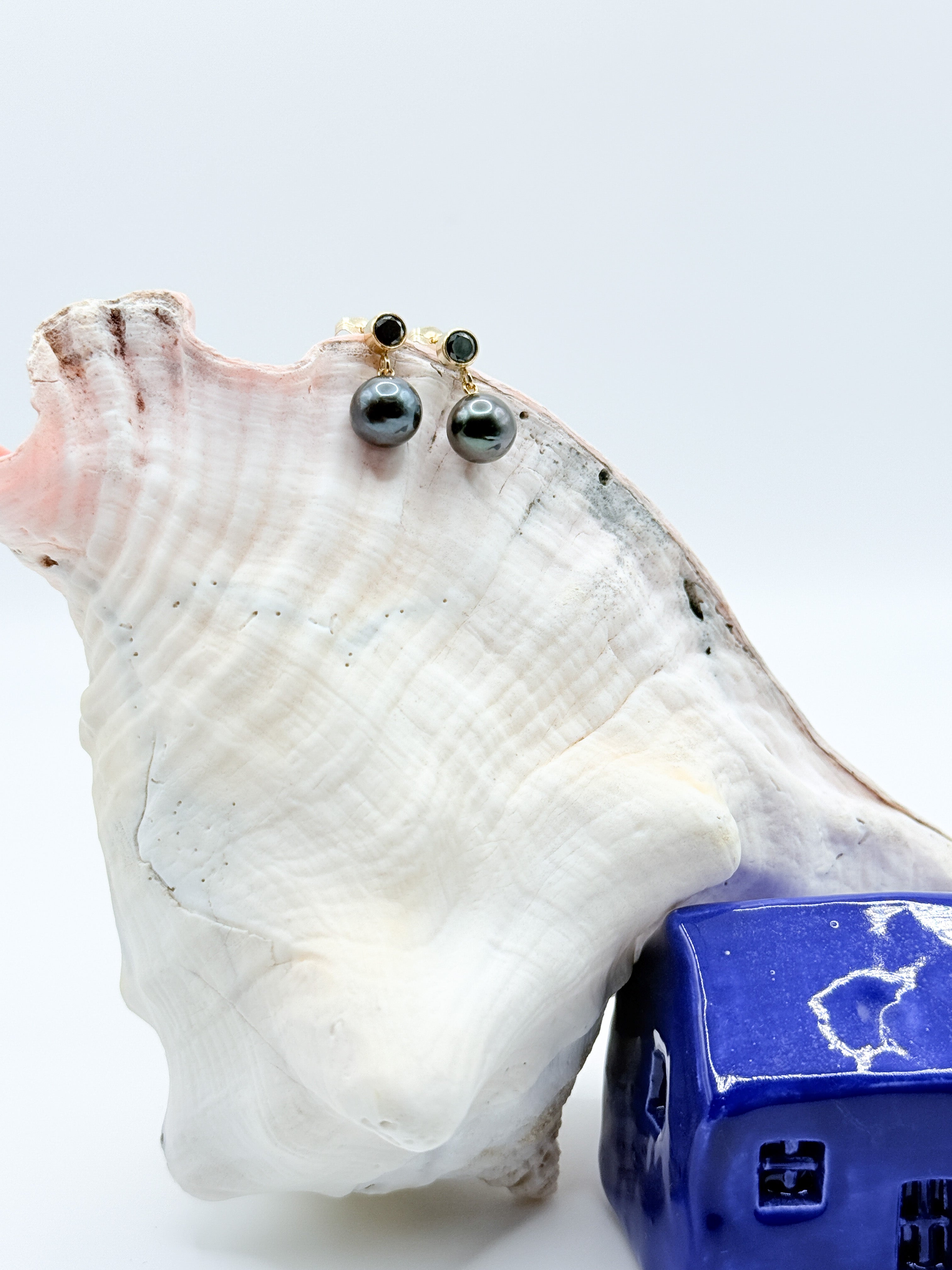 Earrings positioned on large white shell with miniature blue house for scale and styling