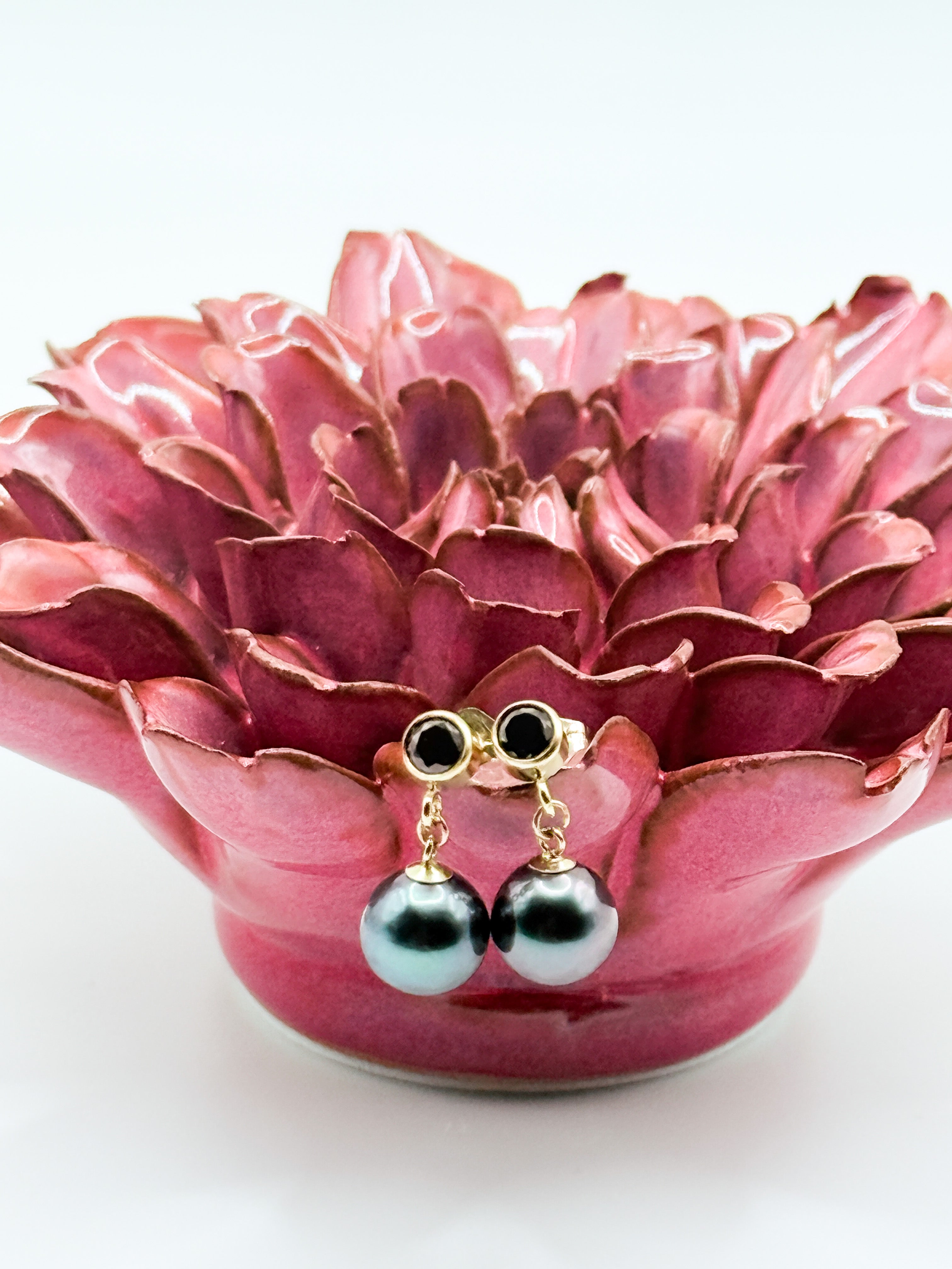 Tahitian pearl drop earrings with black CZ studs displayed on a pink ceramic lotus background
