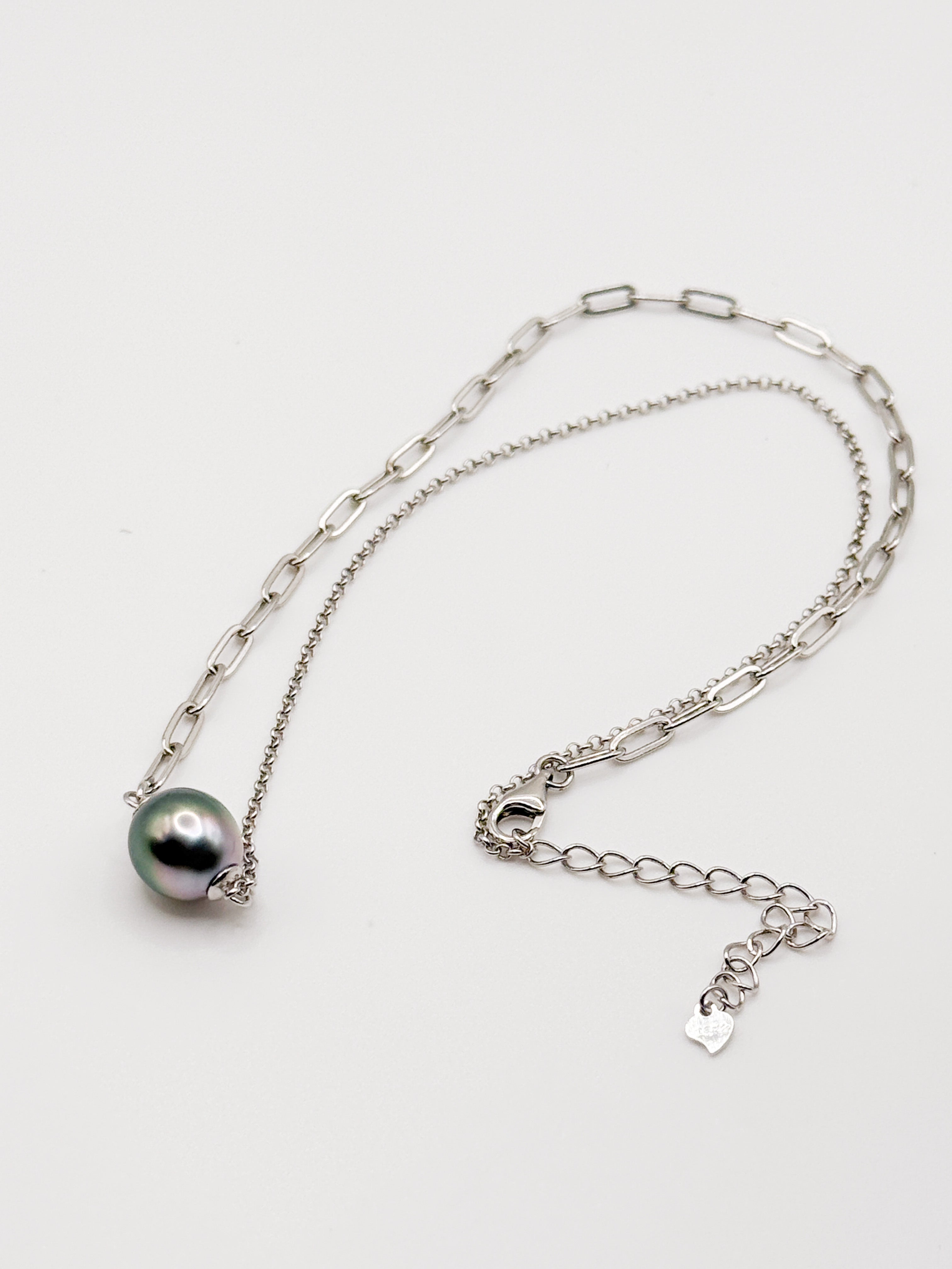 Flat lay of necklace showing floating Tahitian pearl on asymmetrical chain with lobster clasp and heart tag