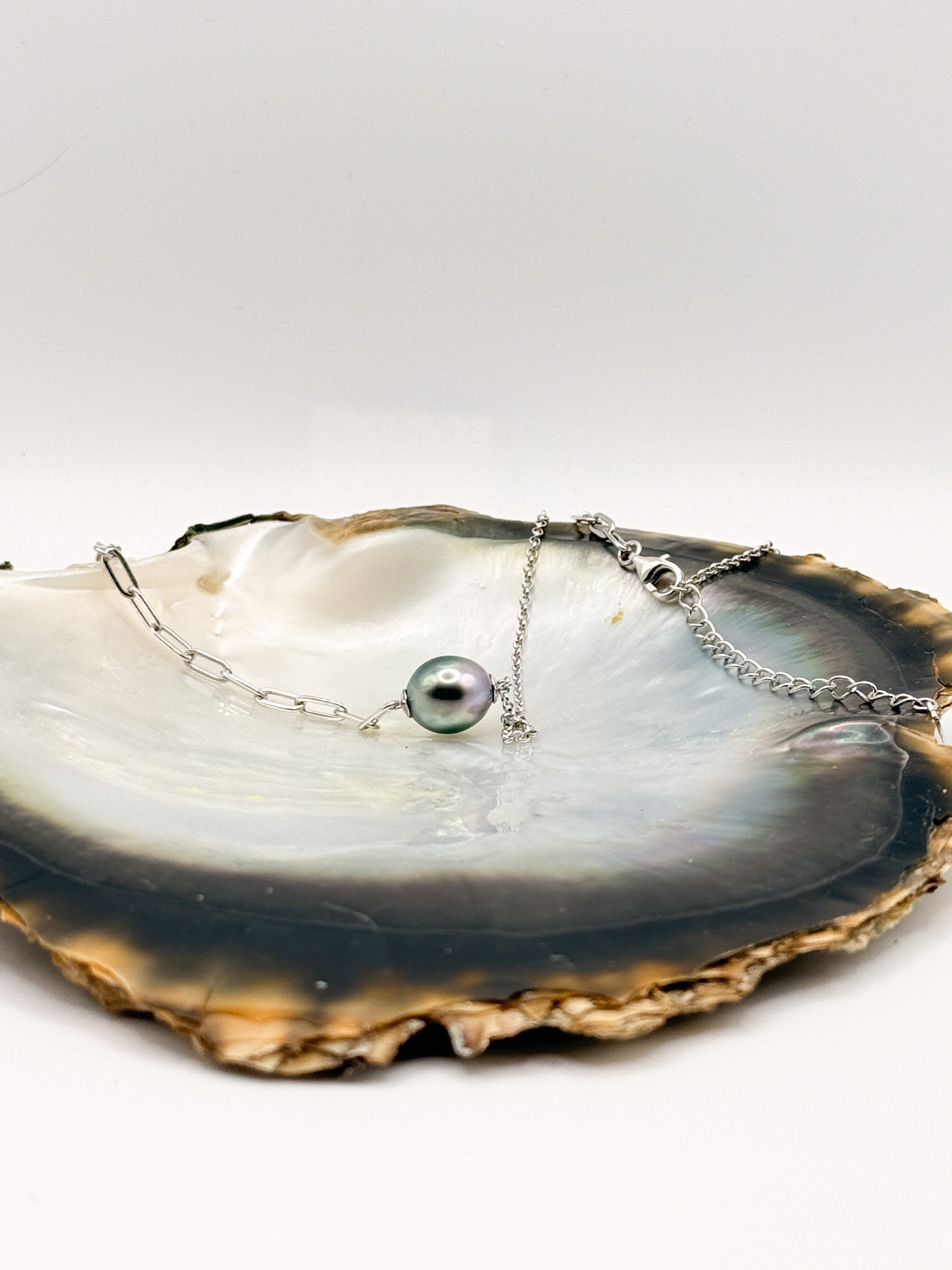 Flat lay of necklace showing floating Tahitian pearl on asymmetrical chain with lobster clasp and heart tag