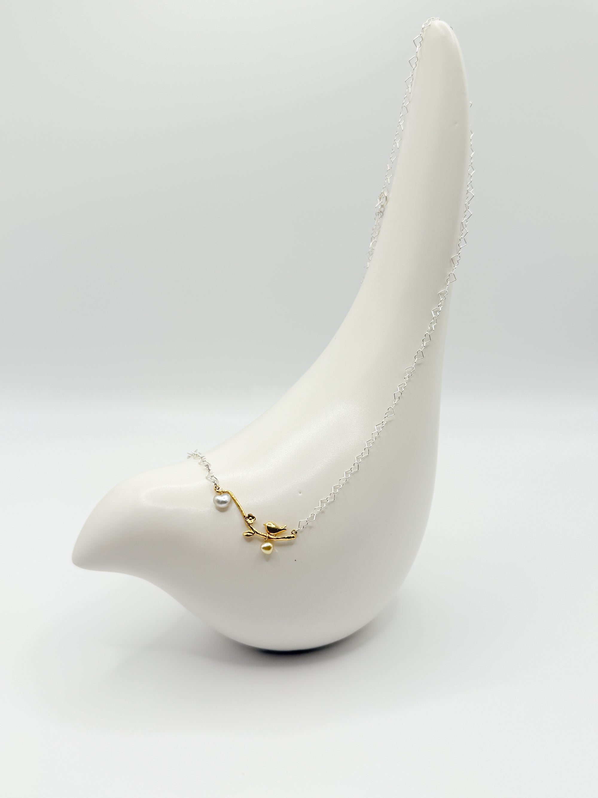 Side view of necklace on white ceramic bird showing heart-shaped Keshi pearls and dainty heart-link chain