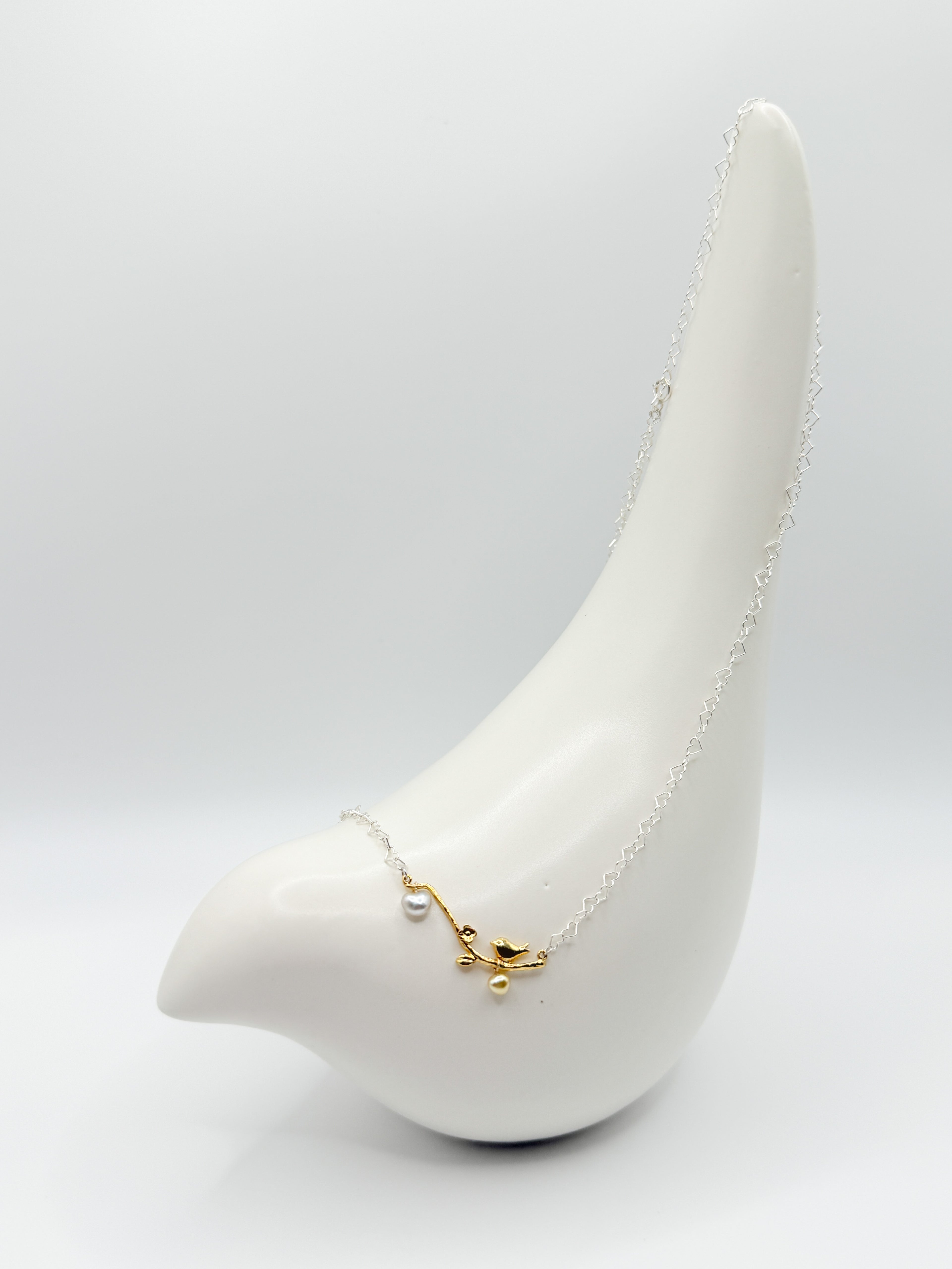Close-up of necklace on ceramic bird showing sculpted gold branch with white and golden heart pearls