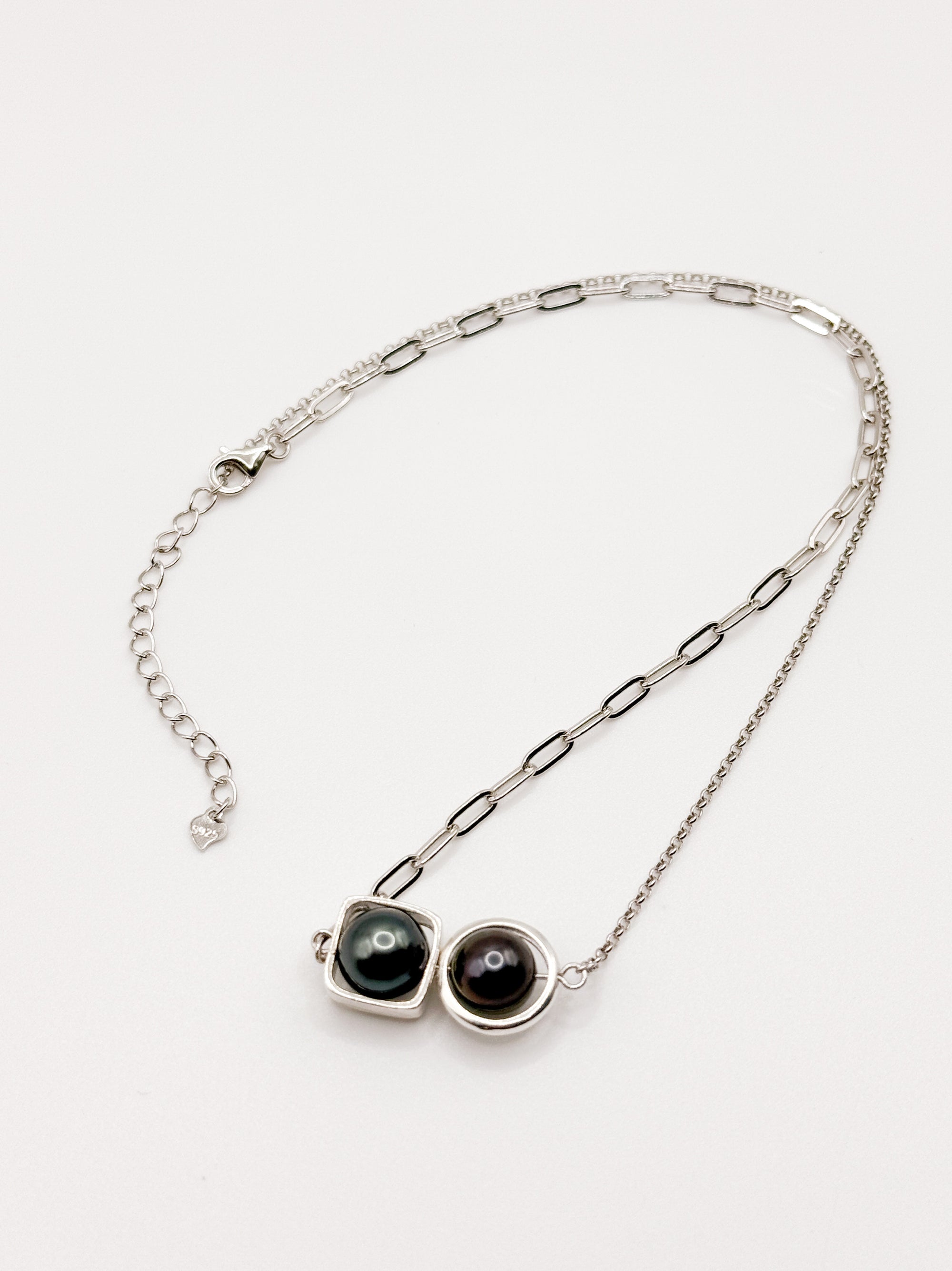 Dual Tahitian pearl necklace with round and square bezels on mixed silver chain laid flat on white background