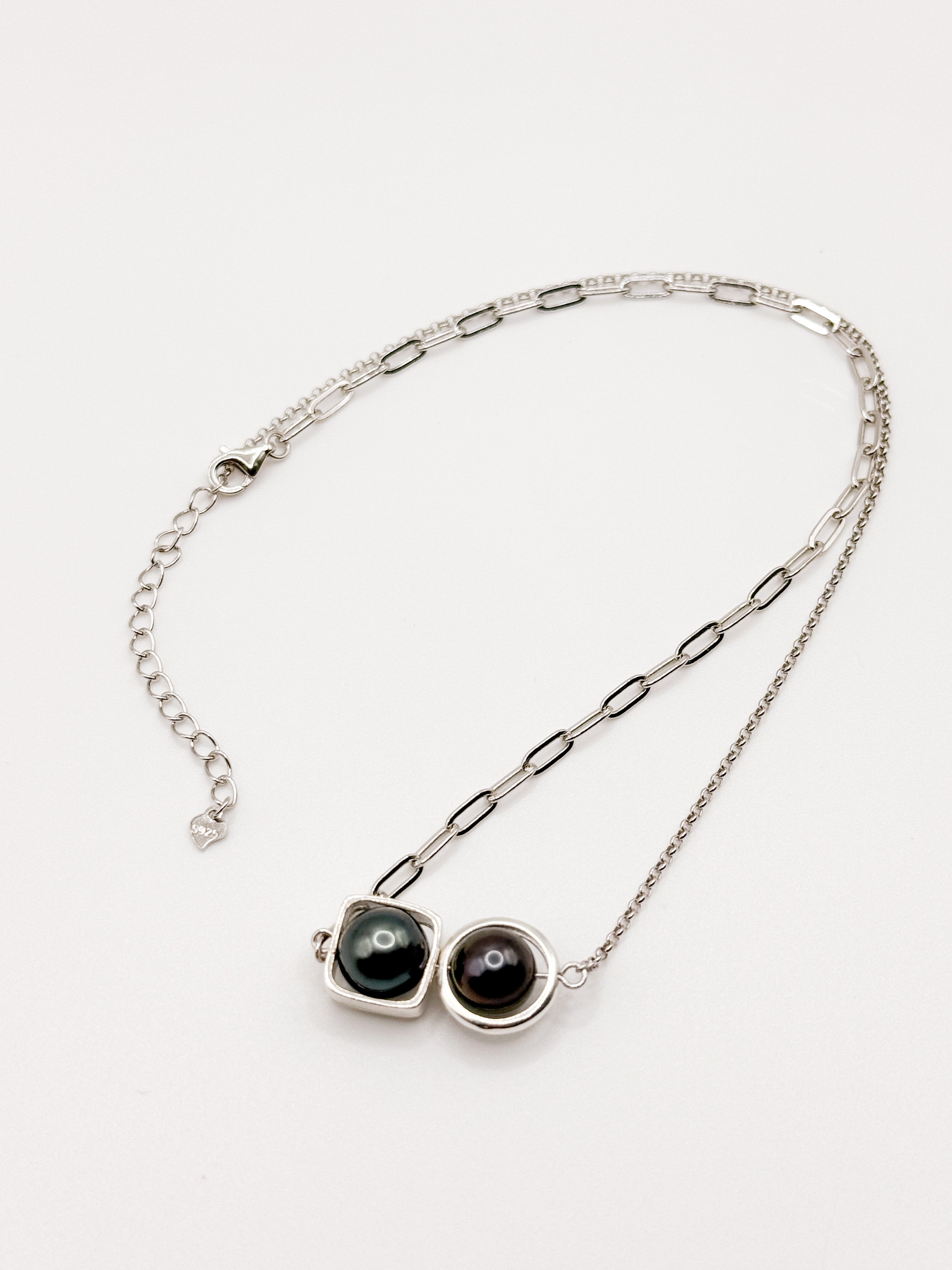 Dual Tahitian pearl necklace with round and square bezels on mixed silver chain laid flat on white background