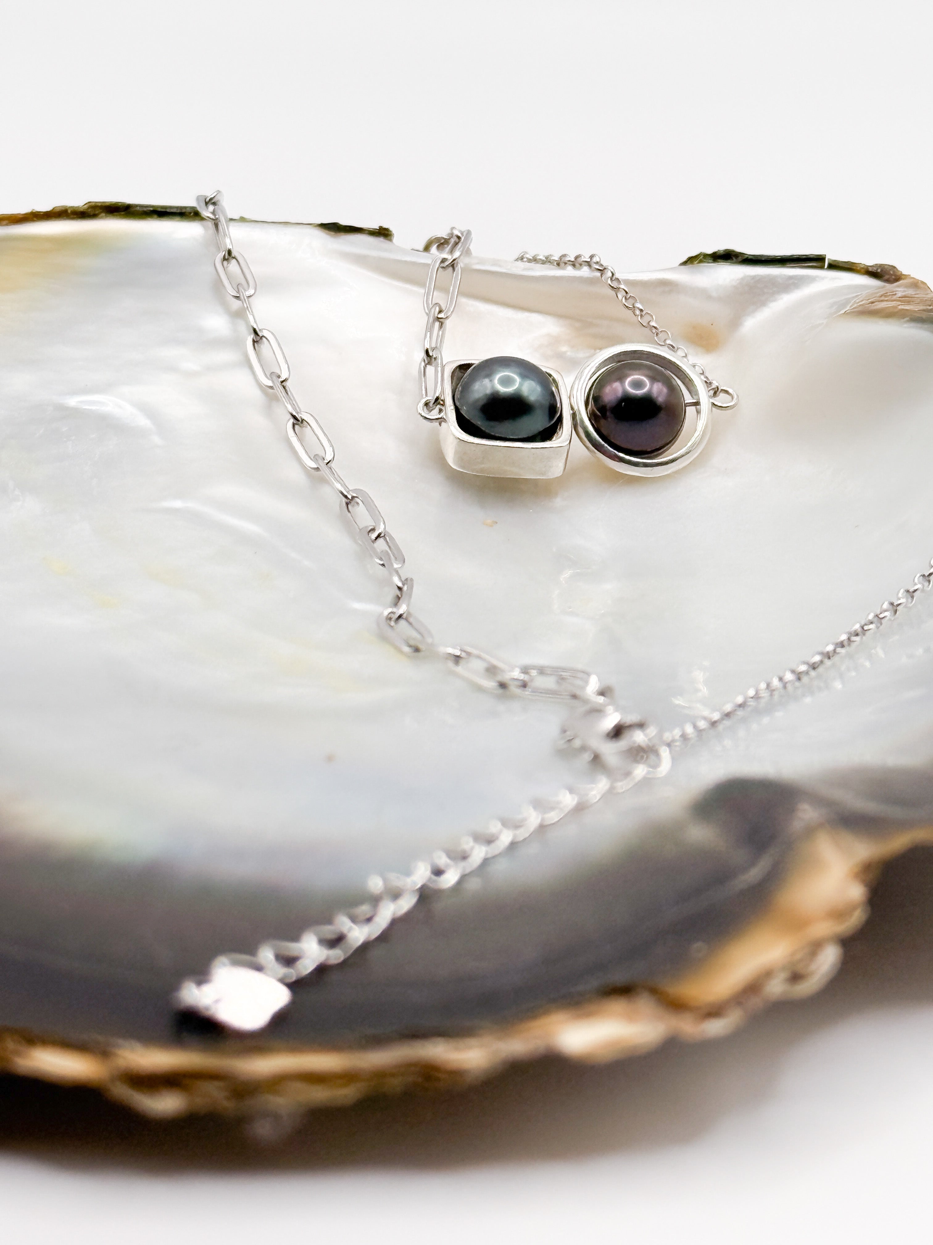 Necklace displayed on mother-of-pearl shell with two bezel-set pearls and silver chain extender visible