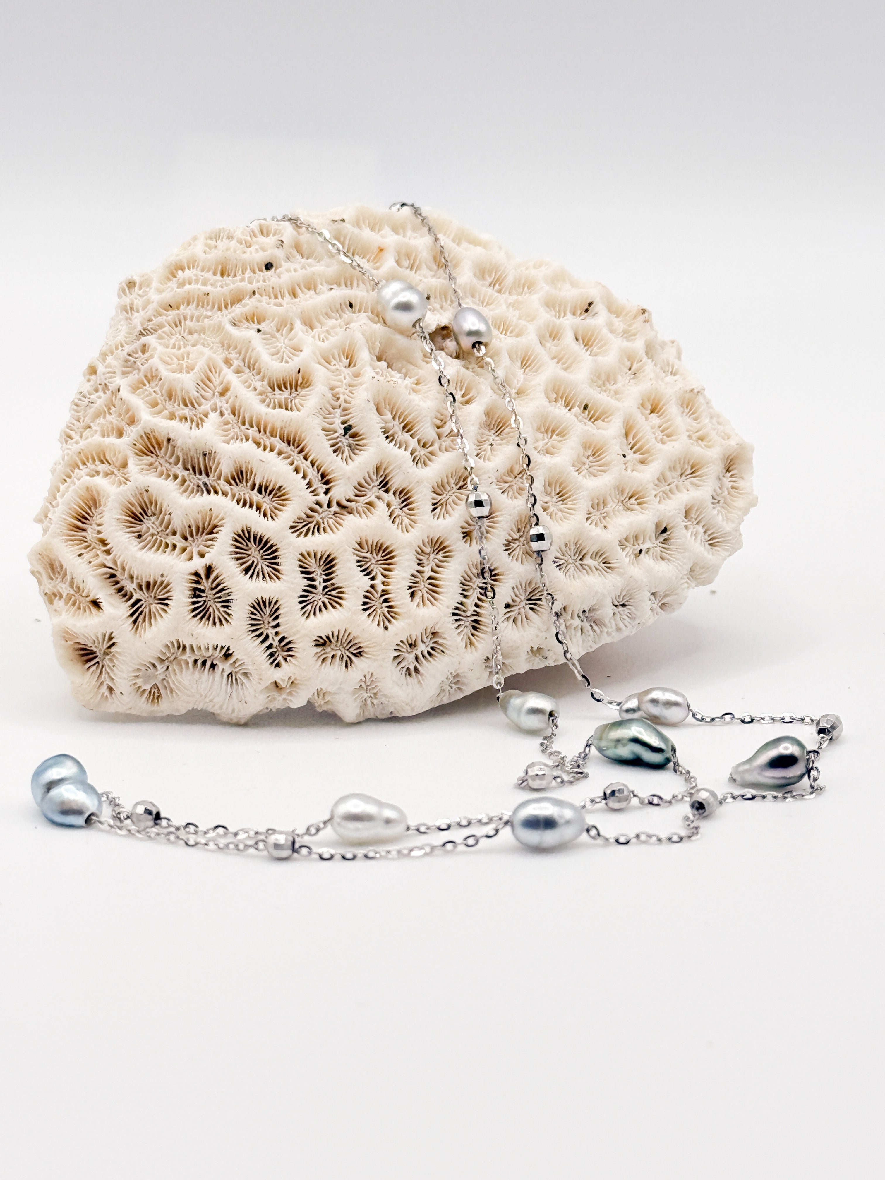 Necklace arranged on coral background showing pearl spacing and fine silver chain details