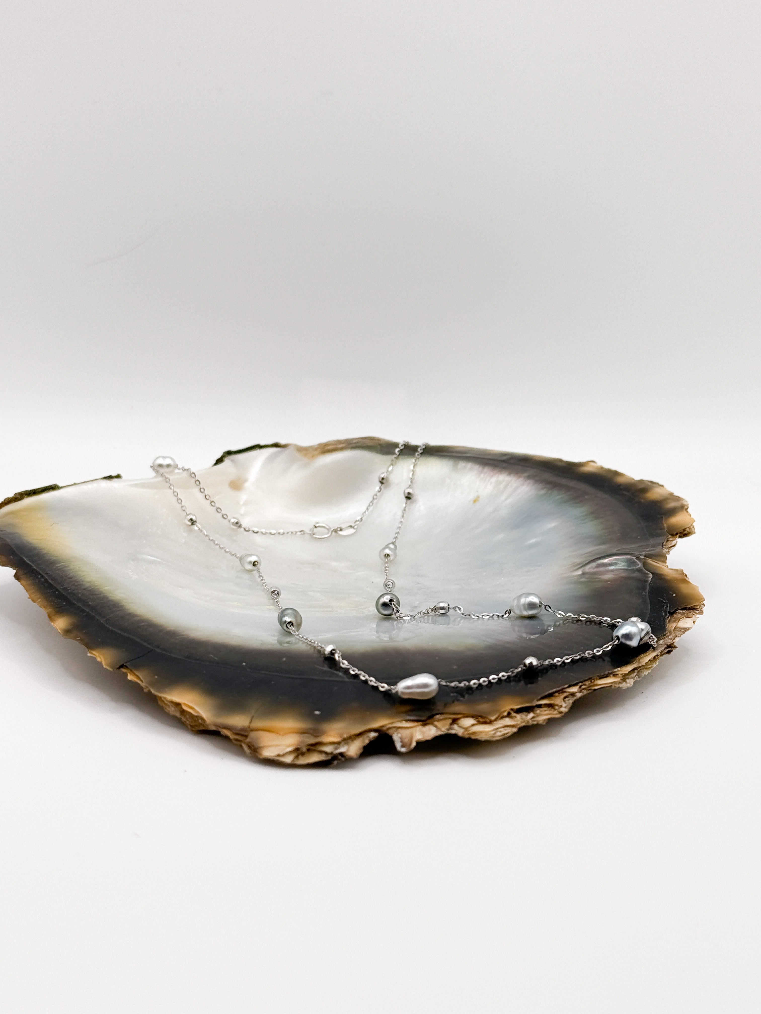 Side view of station necklace placed inside oyster shell highlighting mixed pearls and silver bead accents