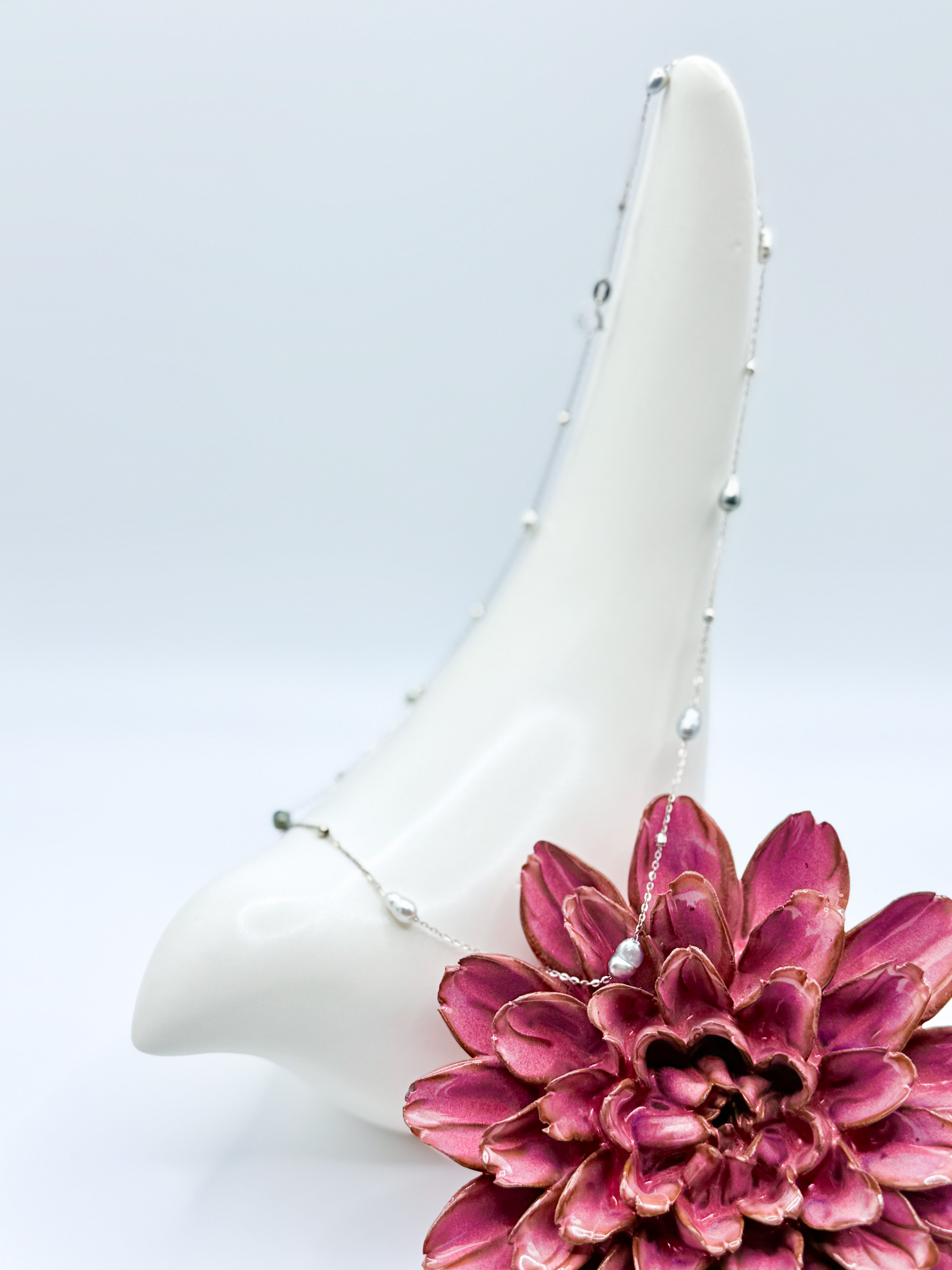 Dainty Tahitian Keshi pearl station necklace draped over ceramic bird and flower prop