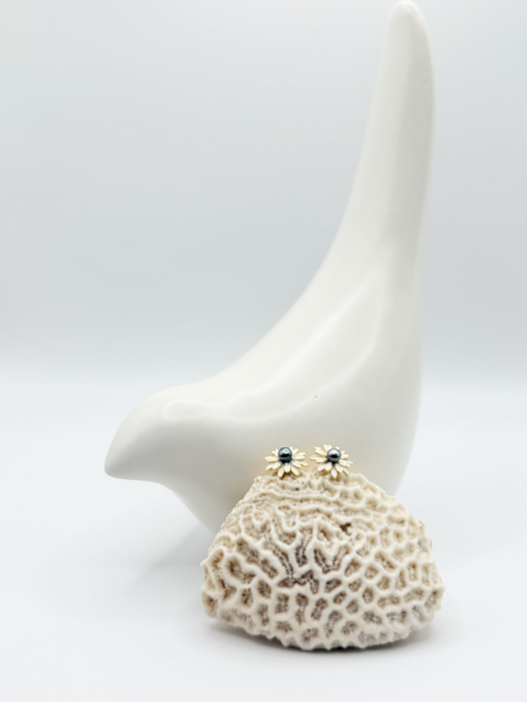 Mini daisy stud earrings with Tahitian blue Keshi pearls displayed on white coral and ceramic bird backdrop