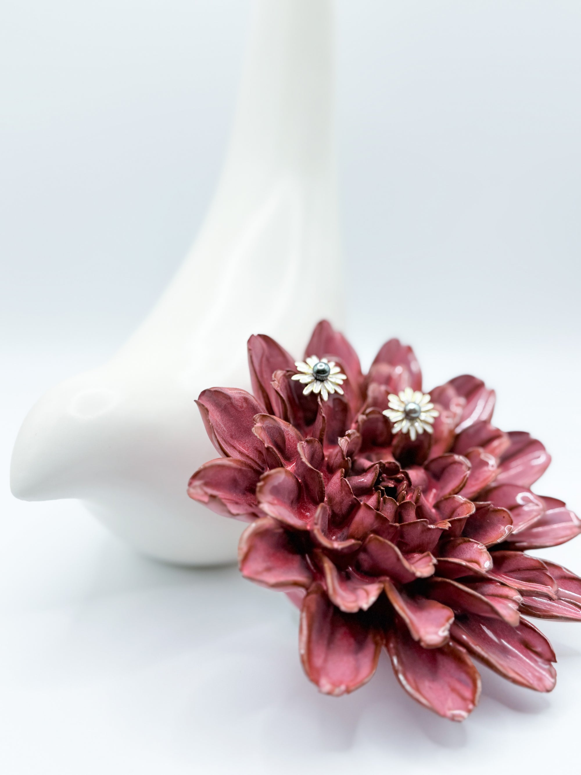 Side angle of earrings nestled in red flower to show dimension and size against organic shapes