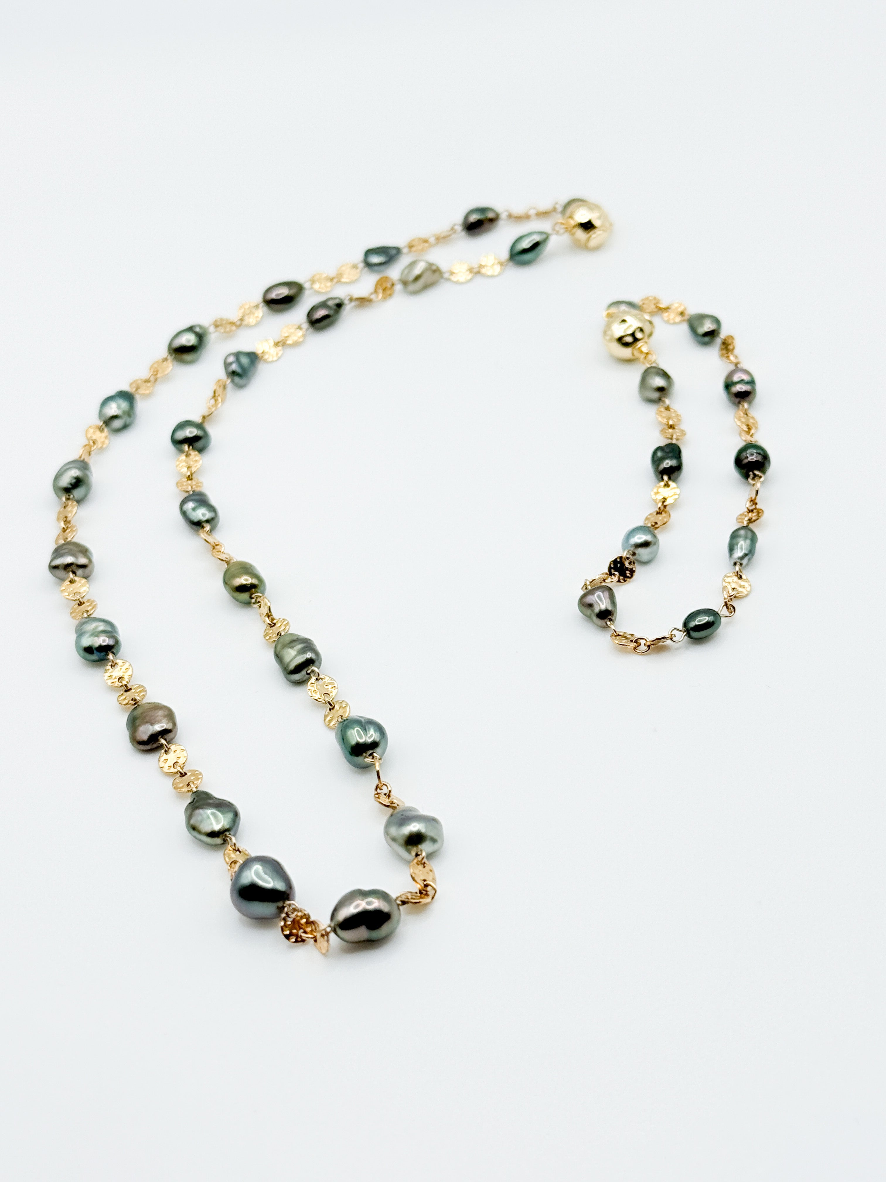 Close-up of necklace laid flat showing irregular dark pearls and detailed gold-filled links