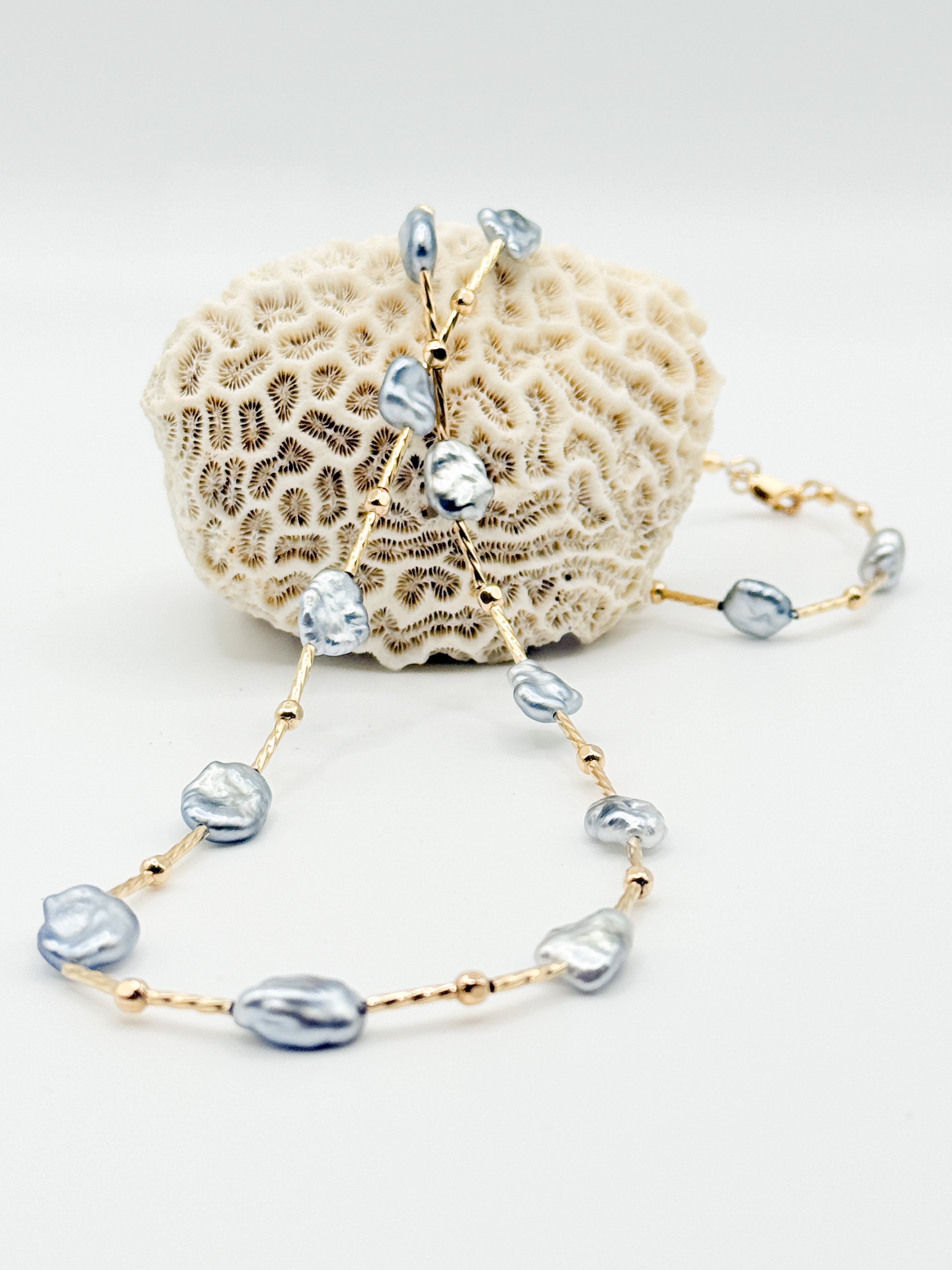 Tahitian Keshi pearl necklace draped on coral, with curved strand in foreground showing lustre and texture.