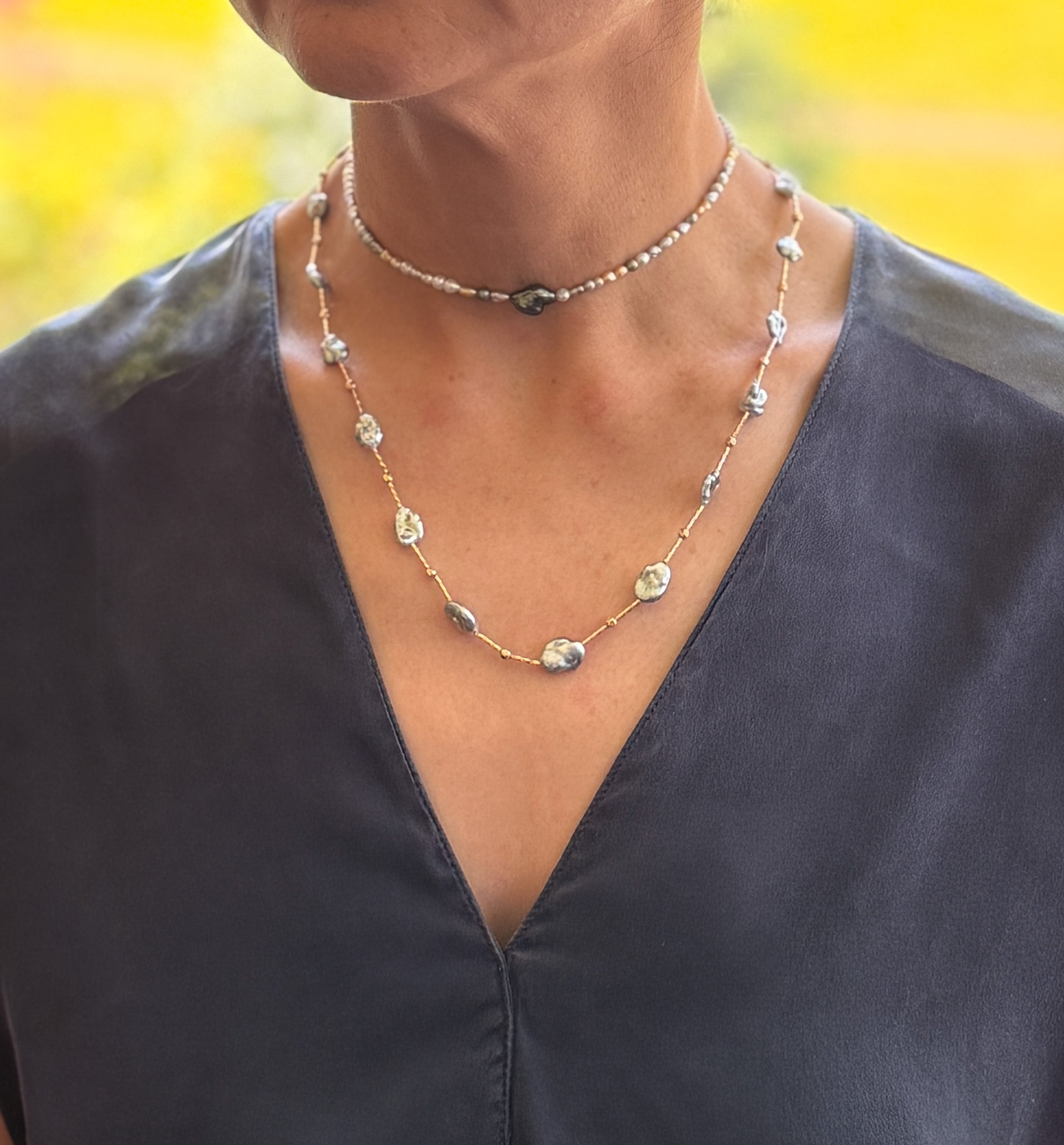 Model wearing blue Tahitian Keshi pearl necklace layered with choker, showing gold-filled station design.