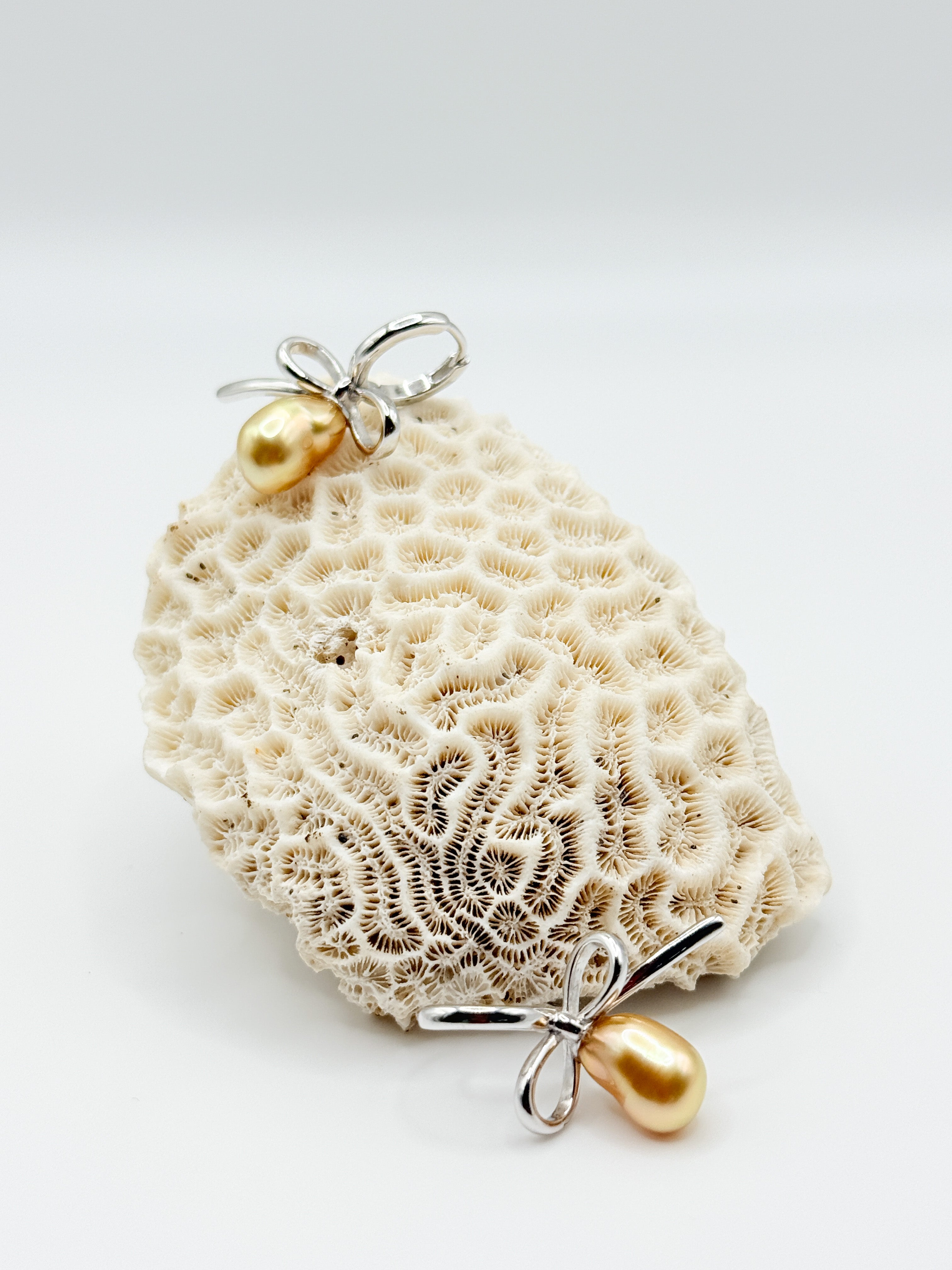 Close-up of golden South Sea Keshi pearl earrings on white coral, highlighting organic pearl shape and silver bow design.
