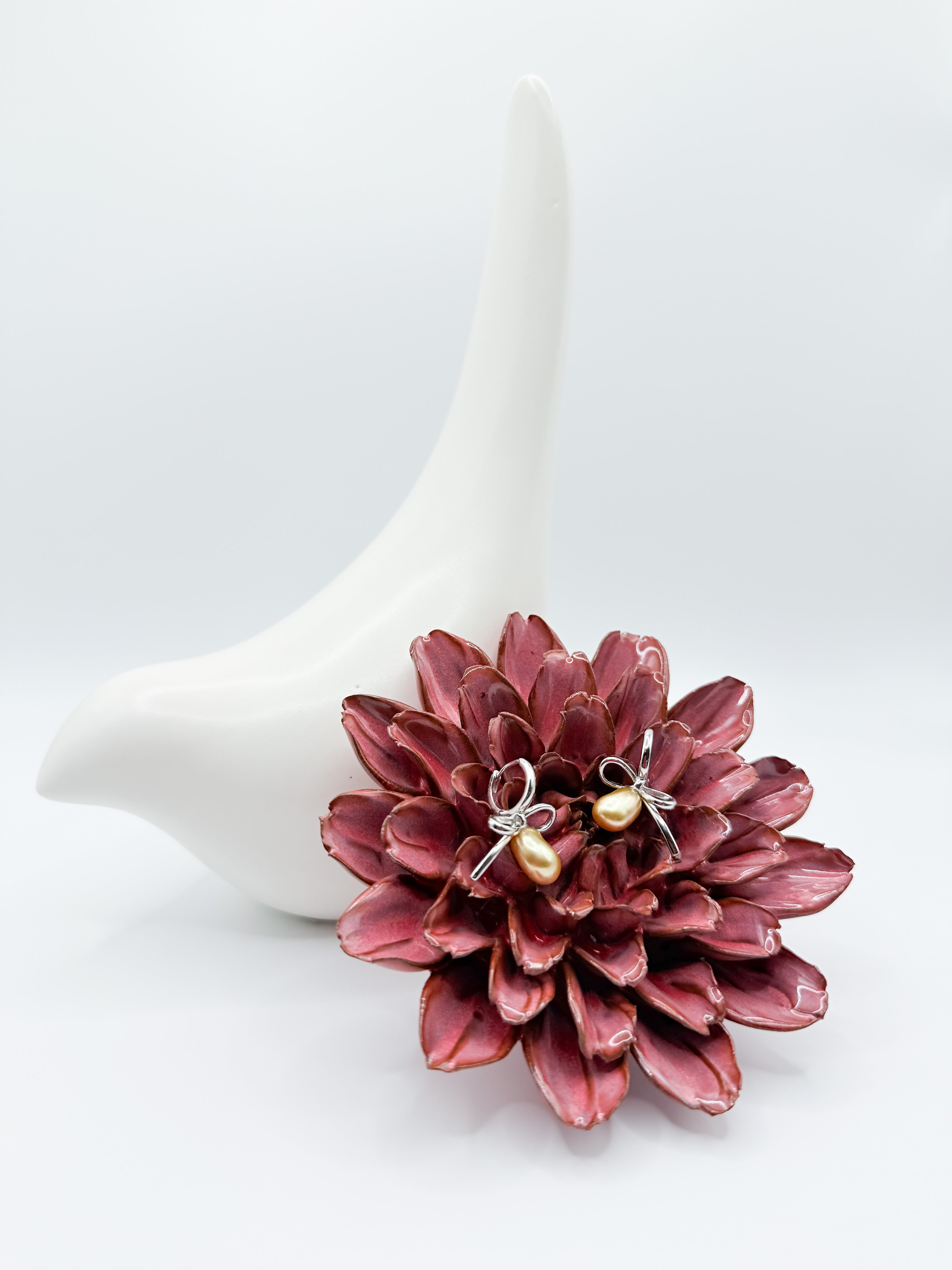Golden South Sea Keshi pearl bow earrings on red flower, showcasing lustrous pearls and 925 silver looped ribbon setting.