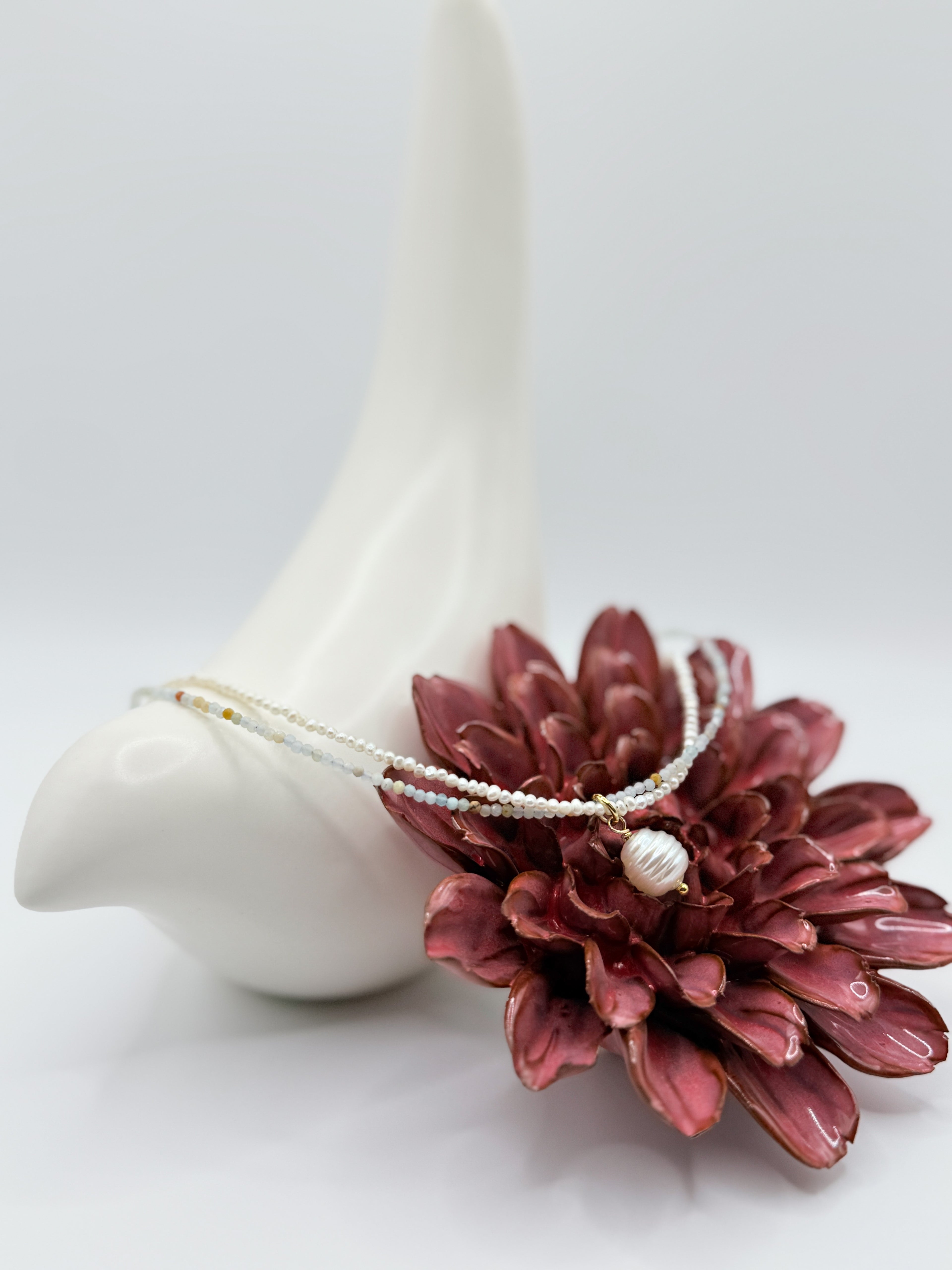 Delicate white pearl choker with seed pearls and pastel amazonite, wrapped around ceramic bird with red flower.