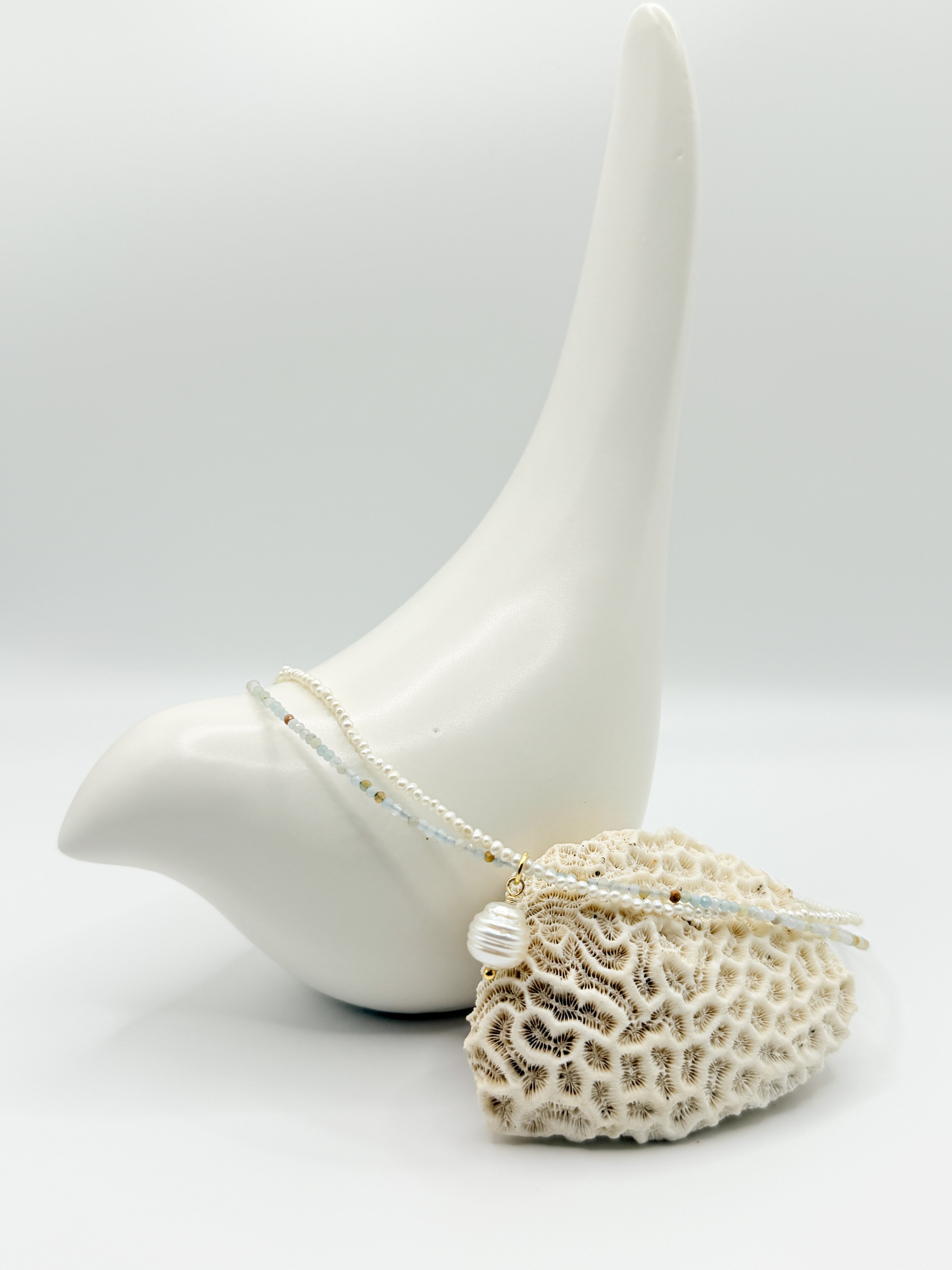 Close-up of South Sea pearl choker resting on coral and ceramic bird, showing fine amazonite and seed pearl details.