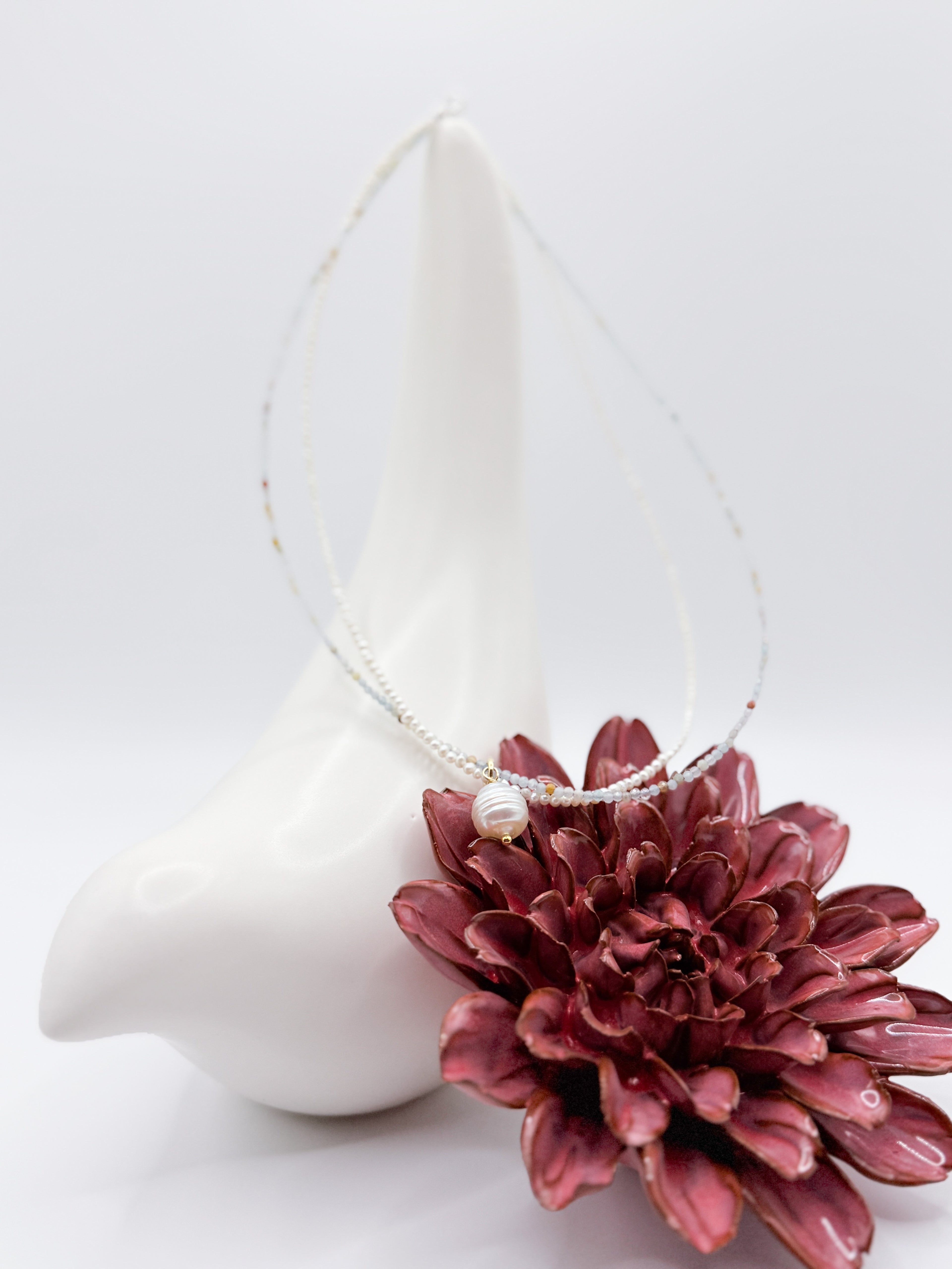 White South Sea pearl choker with seed pearls and amazonite beads, draped over a ceramic bird and red flower.