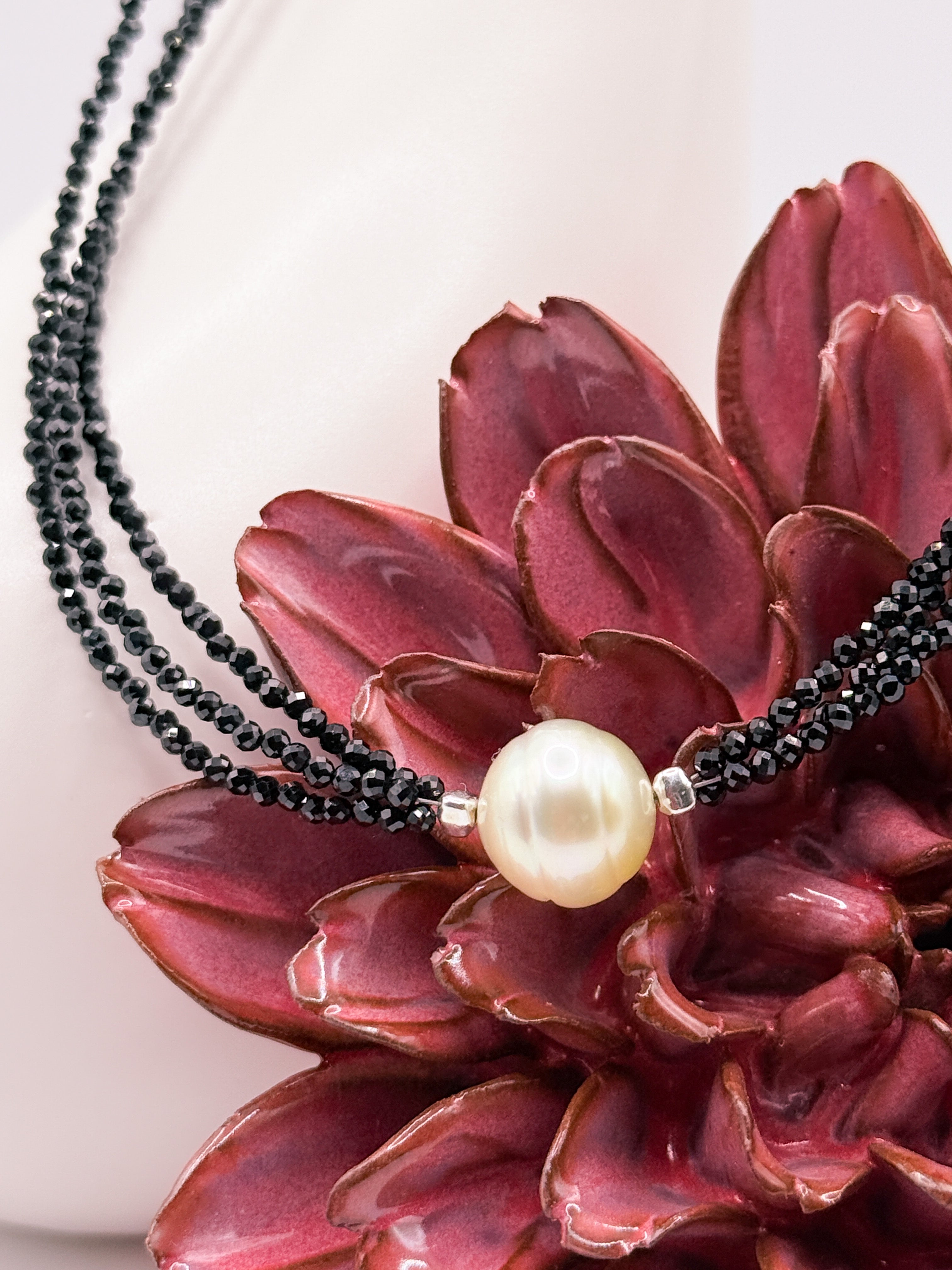 Close-up of South Sea gold pearl on triple black spinel strands, resting on red flower for contrast.