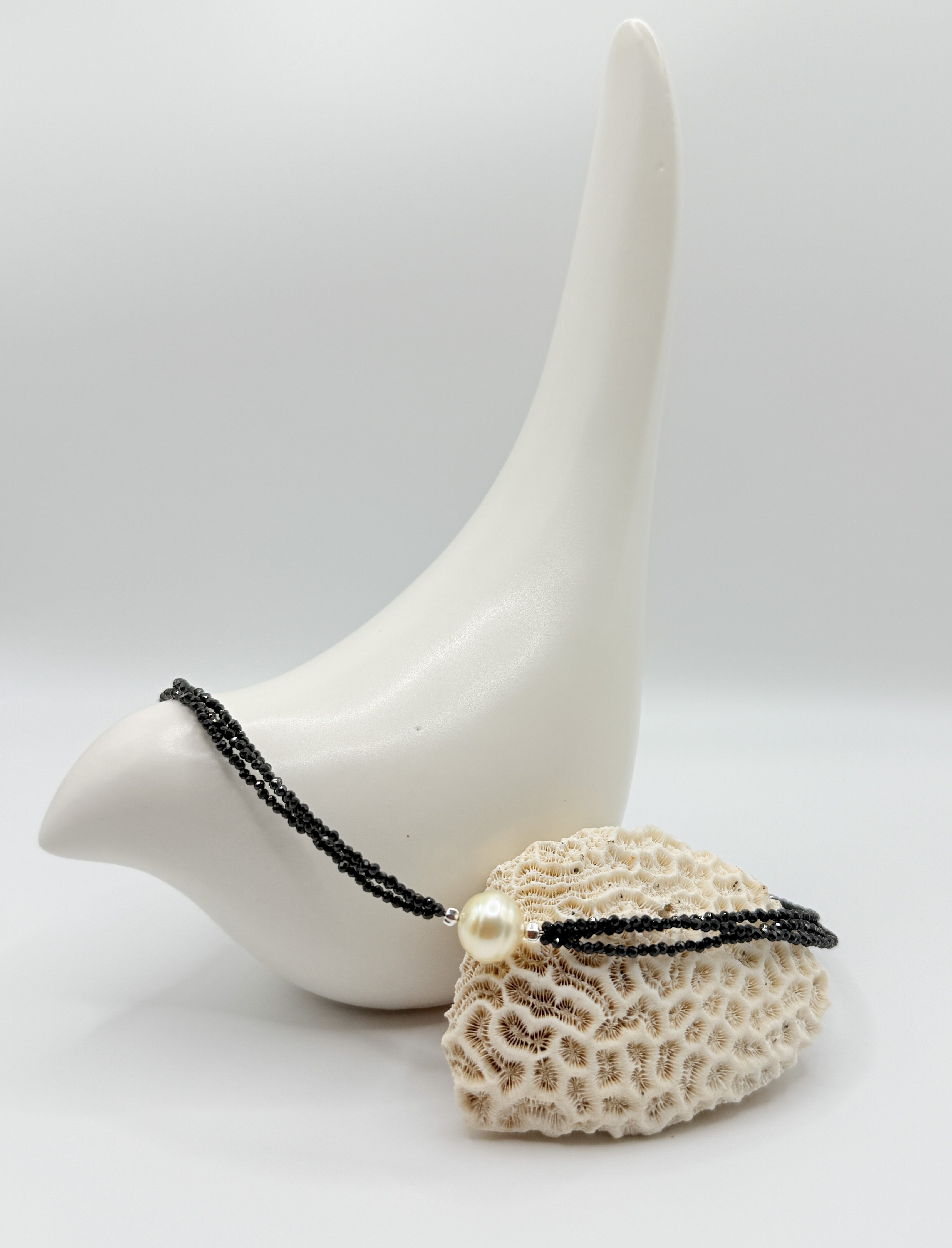 Baroque South Sea gold pearl necklace with faceted black spinel beads, arranged across coral and ceramic bird.