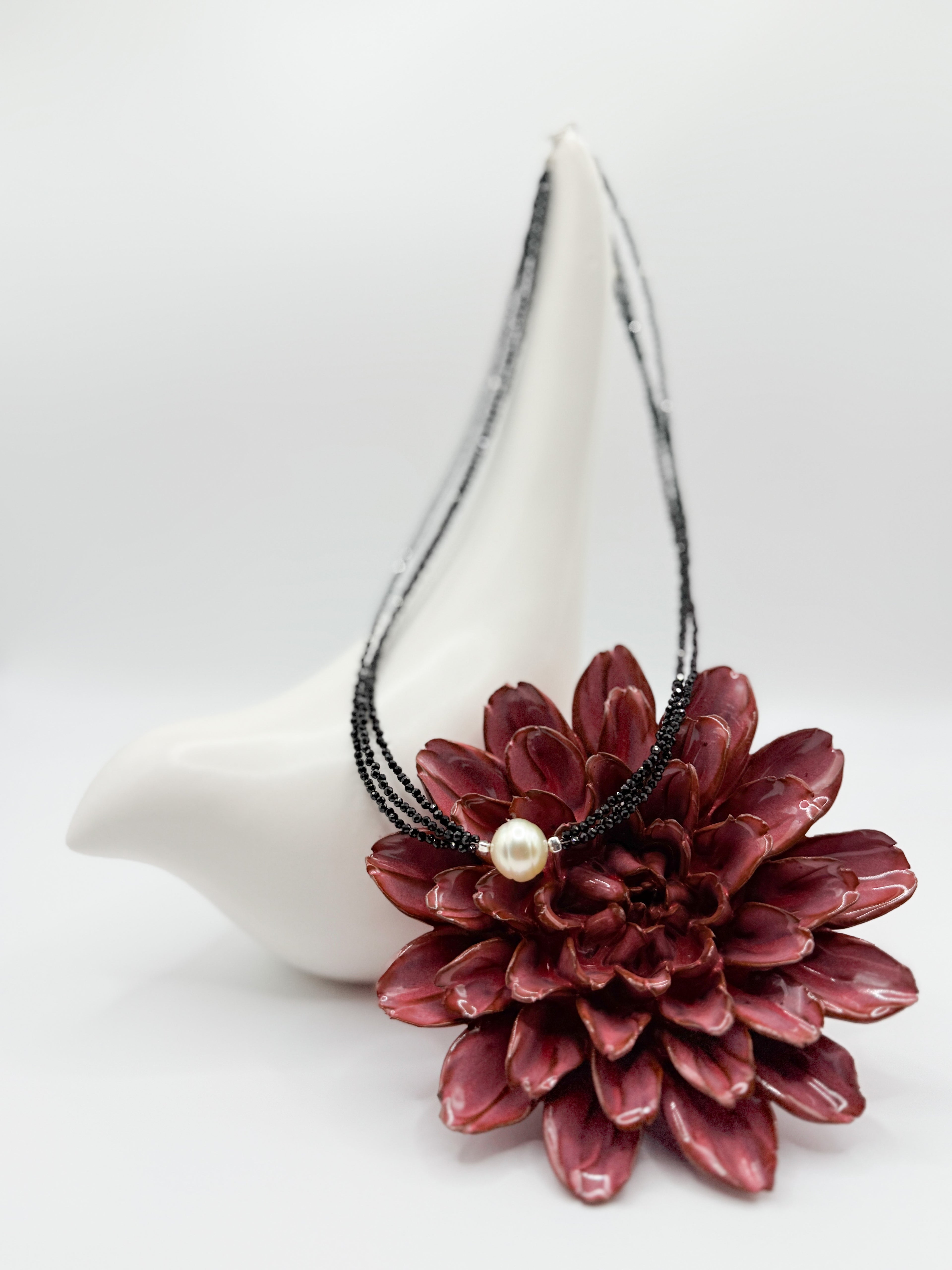Black spinel choker with three strands and central South Sea gold pearl, styled on ceramic bird with red flower.