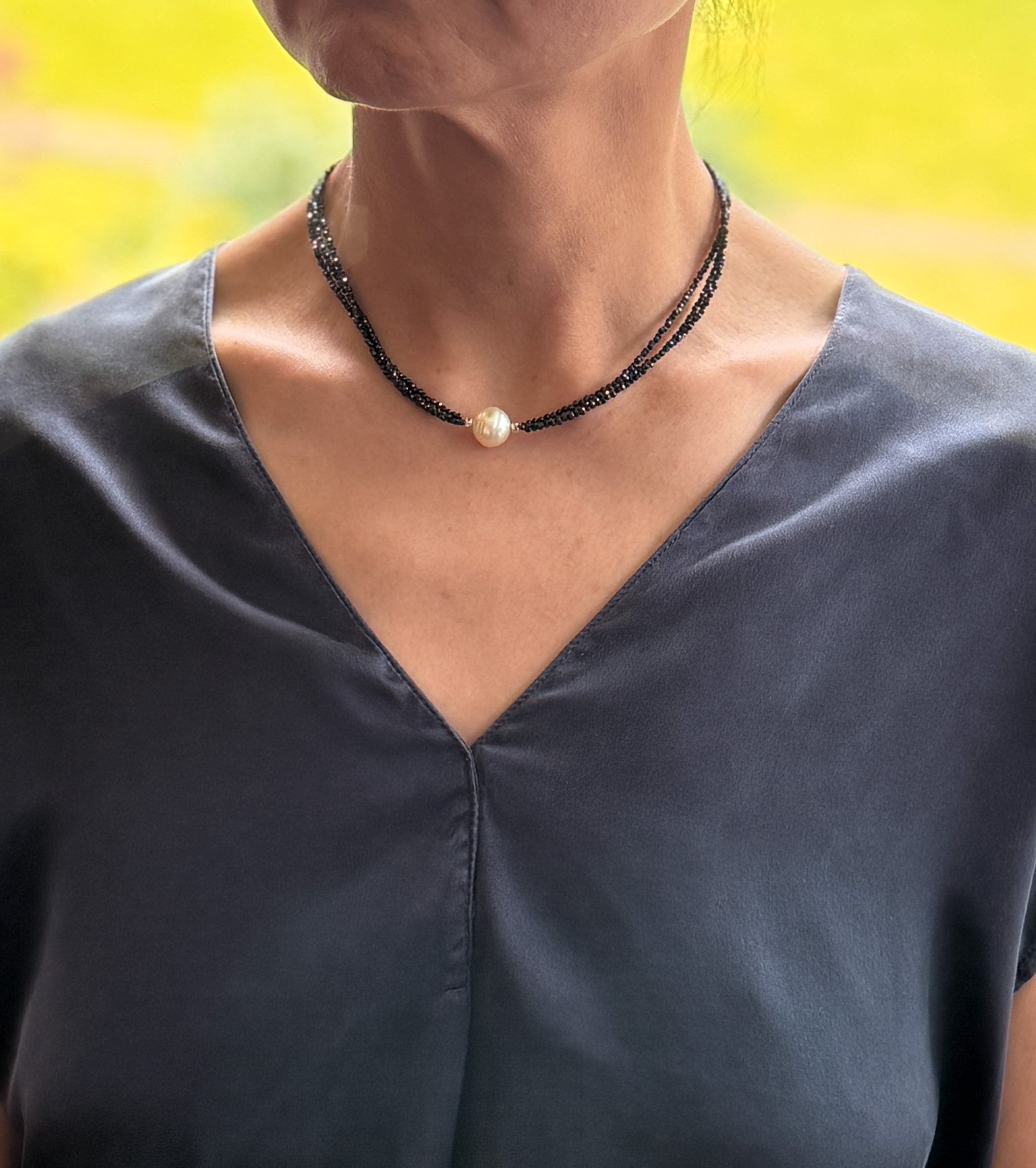 Model wearing 3-strand black spinel choker with luminous South Sea pearl, styled against a deep neckline.