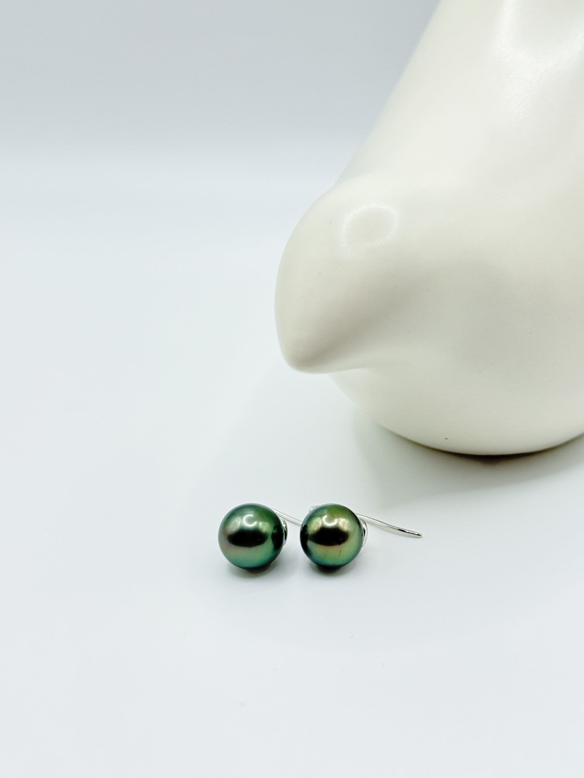Tahitian pearl earrings resting on white background with ceramic bird, showcasing round shape and orient.