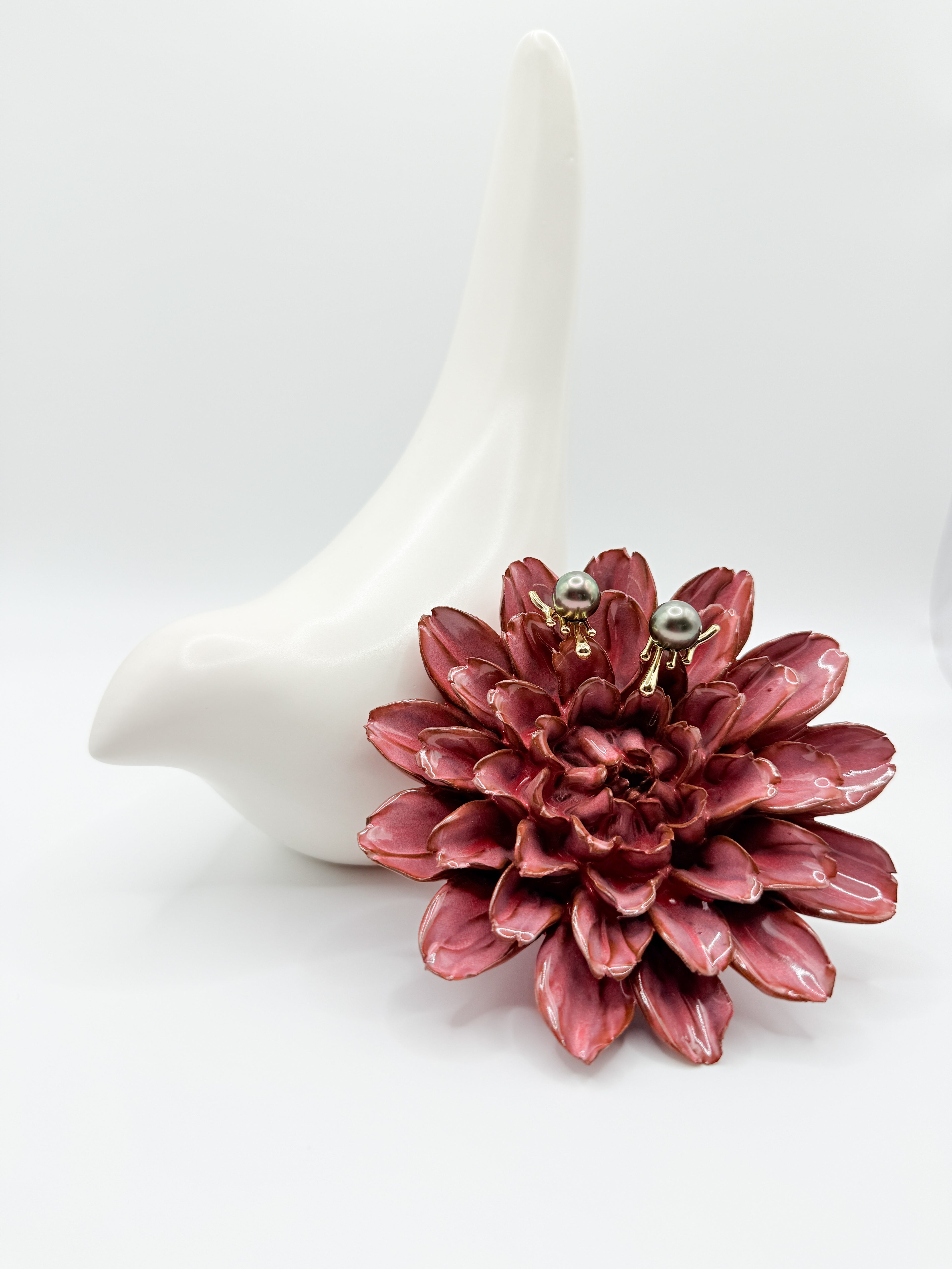 Tahitian pearl studs displayed on red flower and ceramic bird, showing molten-effect 925 silver detail.