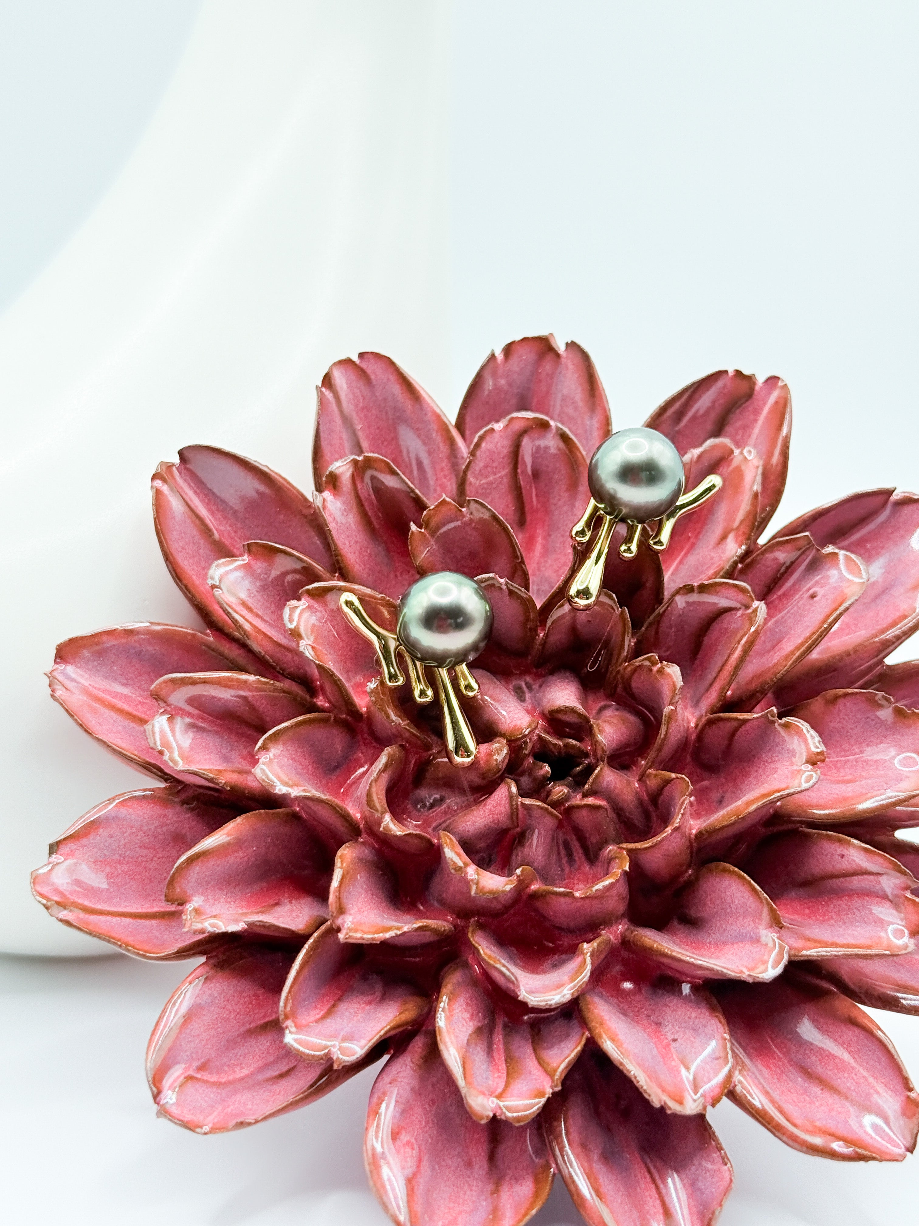 Close-up of green Tahitian pearl earrings in organic molten silver setting, styled on red flower.