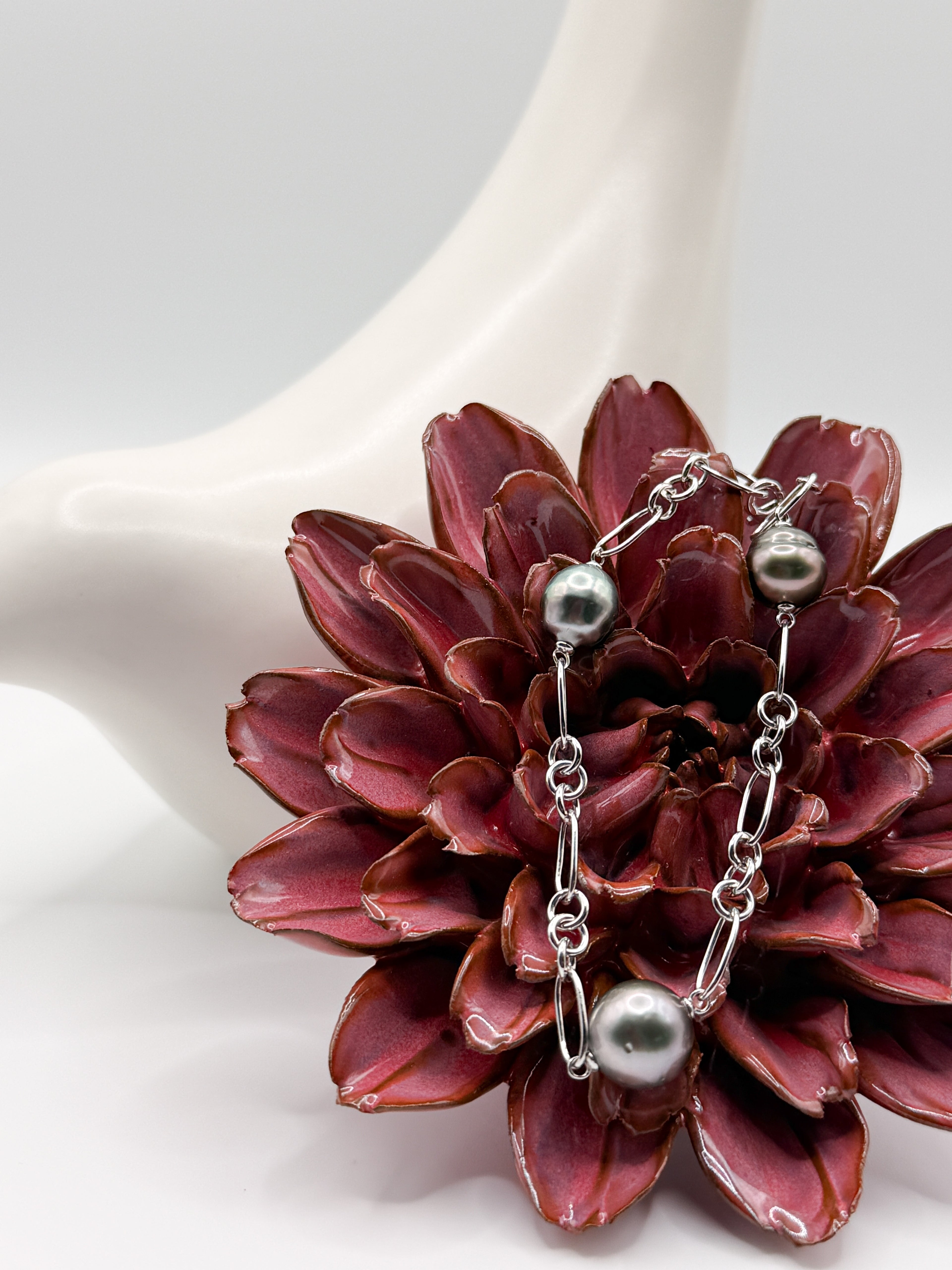Three-pearl Tahitian bracelet in silver Figaro chain, draped over red flower sculpture for layered texture contrast.