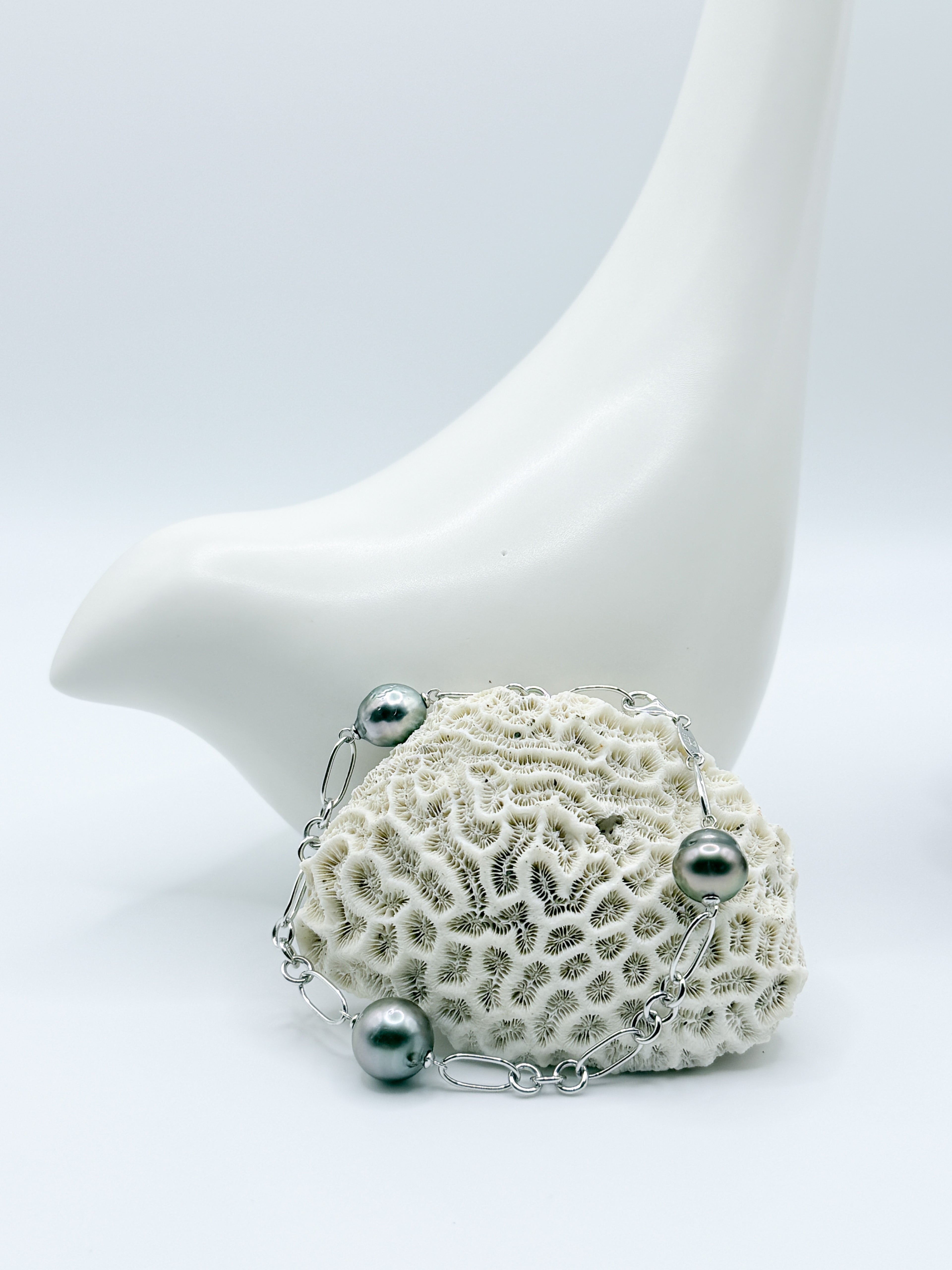 Tahitian baroque pearl bracelet laid over coral, showing 925 silver Figaro chain links and natural pearl forms.