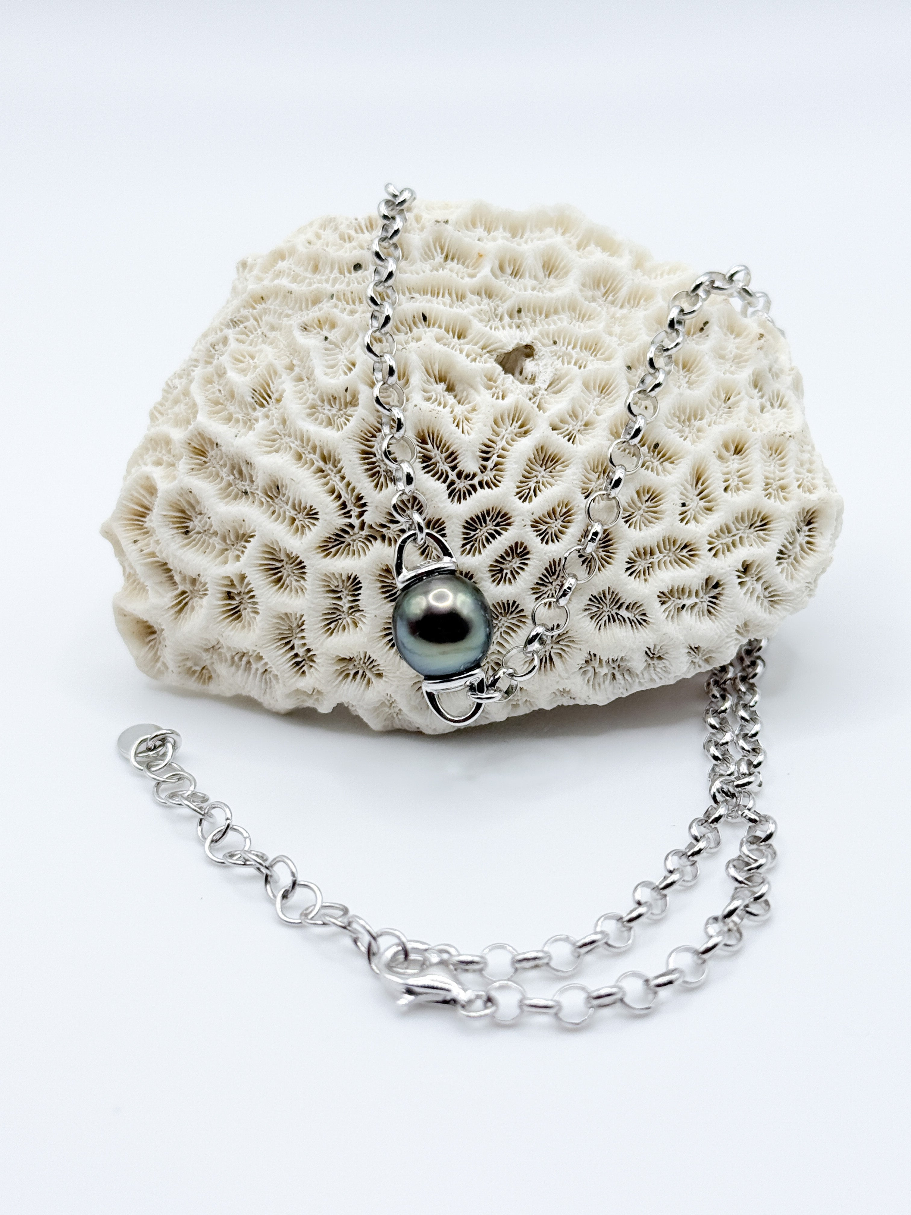 Floating Tahitian pearl pendant necklace displayed on coral, showing polished sterling silver chain and clasp.