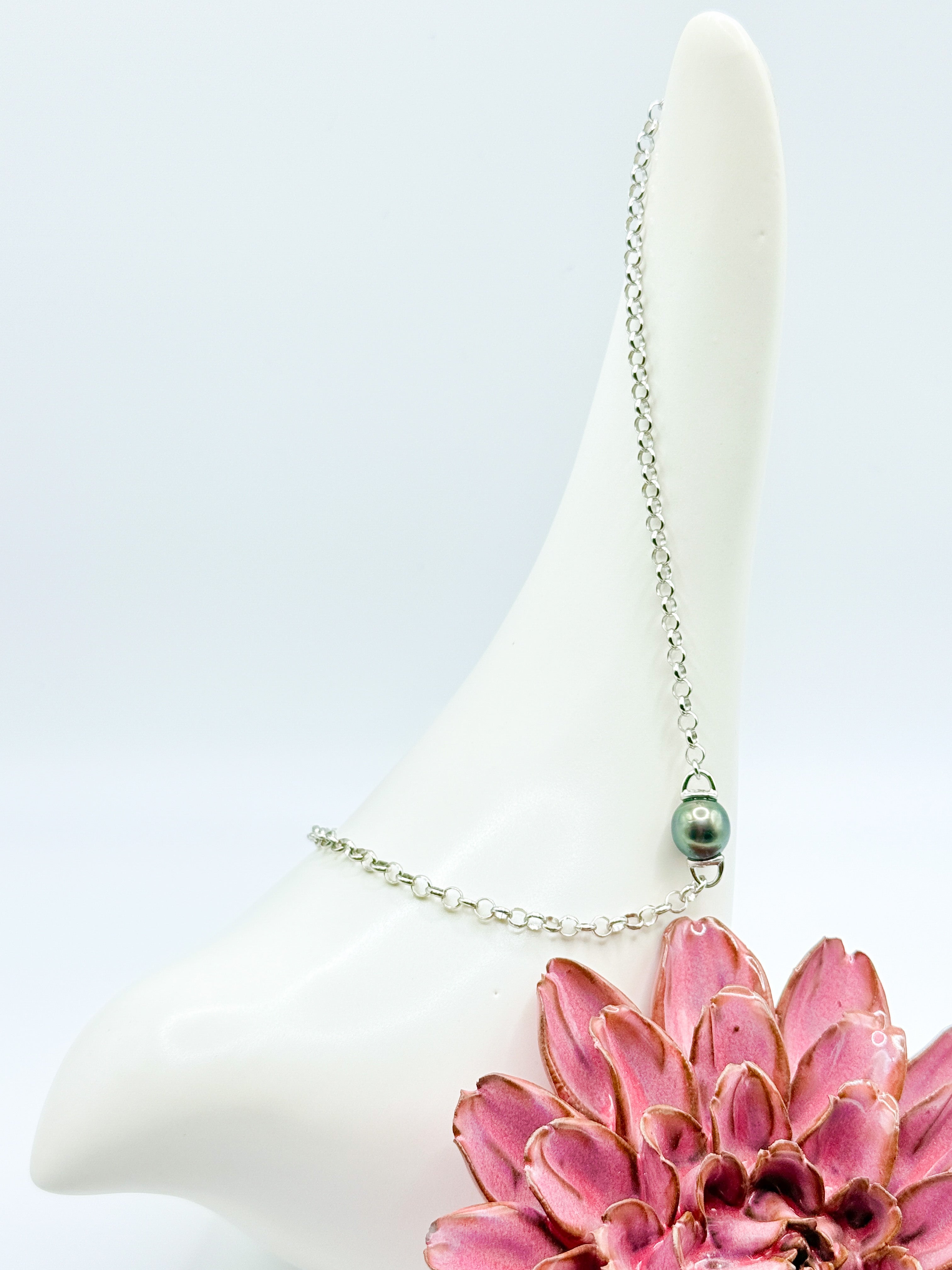 Close-up of baroque Tahitian pearl on sterling silver chain, styled with ceramic bird and red flower accent.