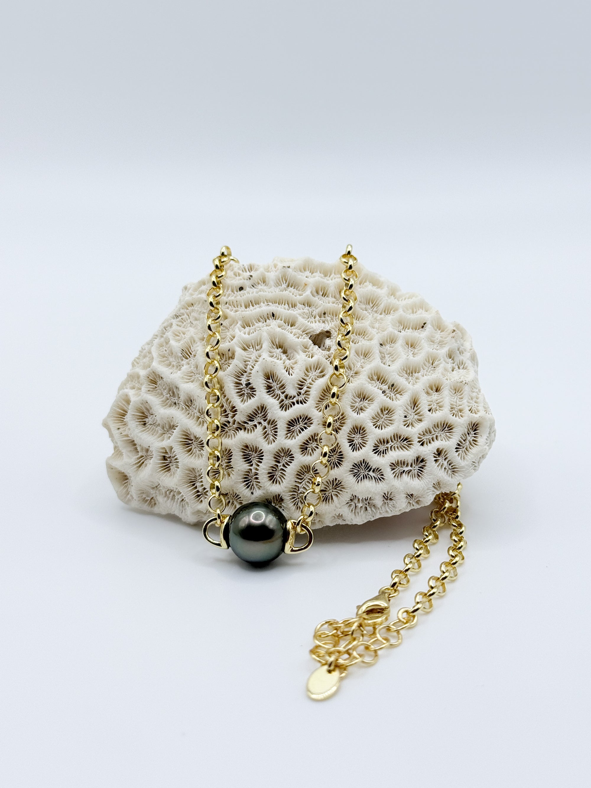 Floating Tahitian pearl pendant necklace displayed on coral, showing polished sterling silver chain and clasp.