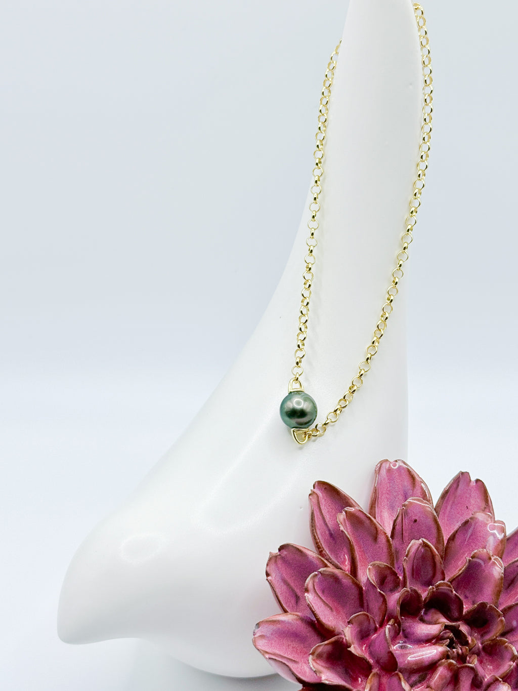 Close-up of baroque Tahitian pearl on sterling silver chain, styled with ceramic bird and red flower accent.