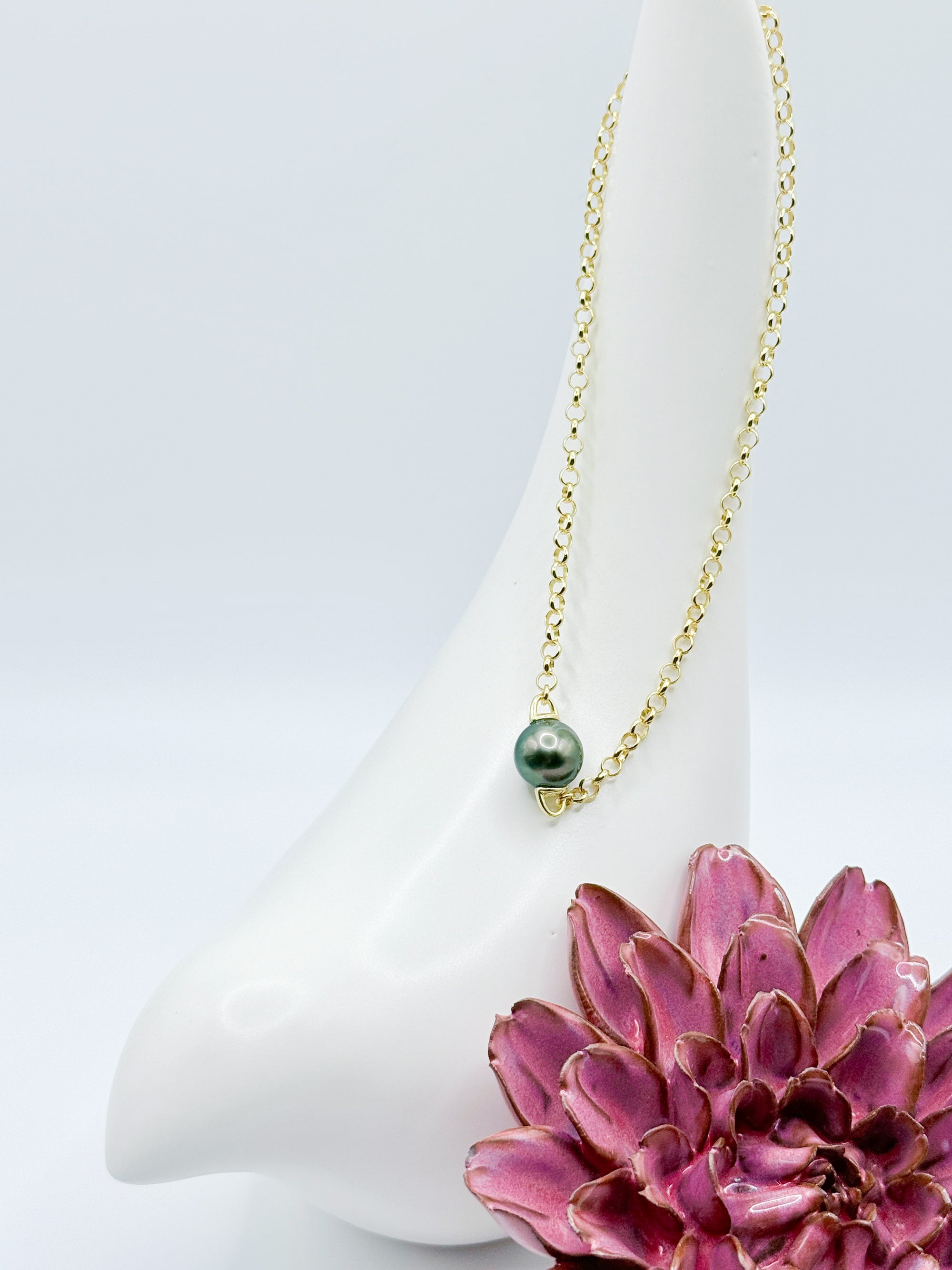Close-up of baroque Tahitian pearl on sterling silver chain, styled with ceramic bird and red flower accent.