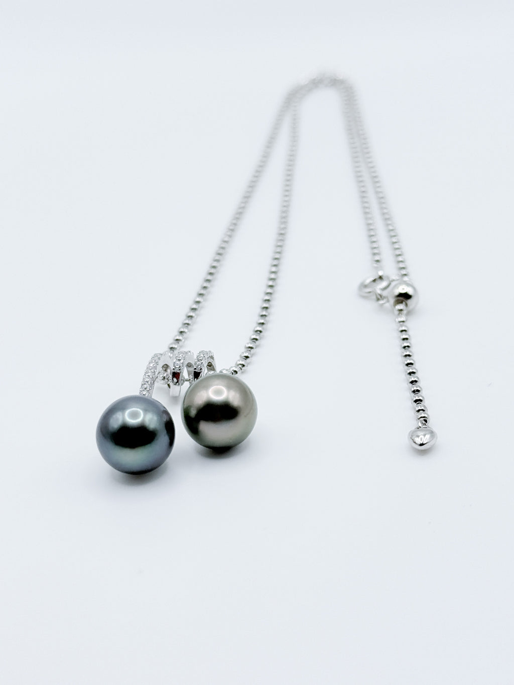 Double Tahitian pearl pendant necklace laid flat, showing sparkling CZ bail and adjustable silver ball chain.