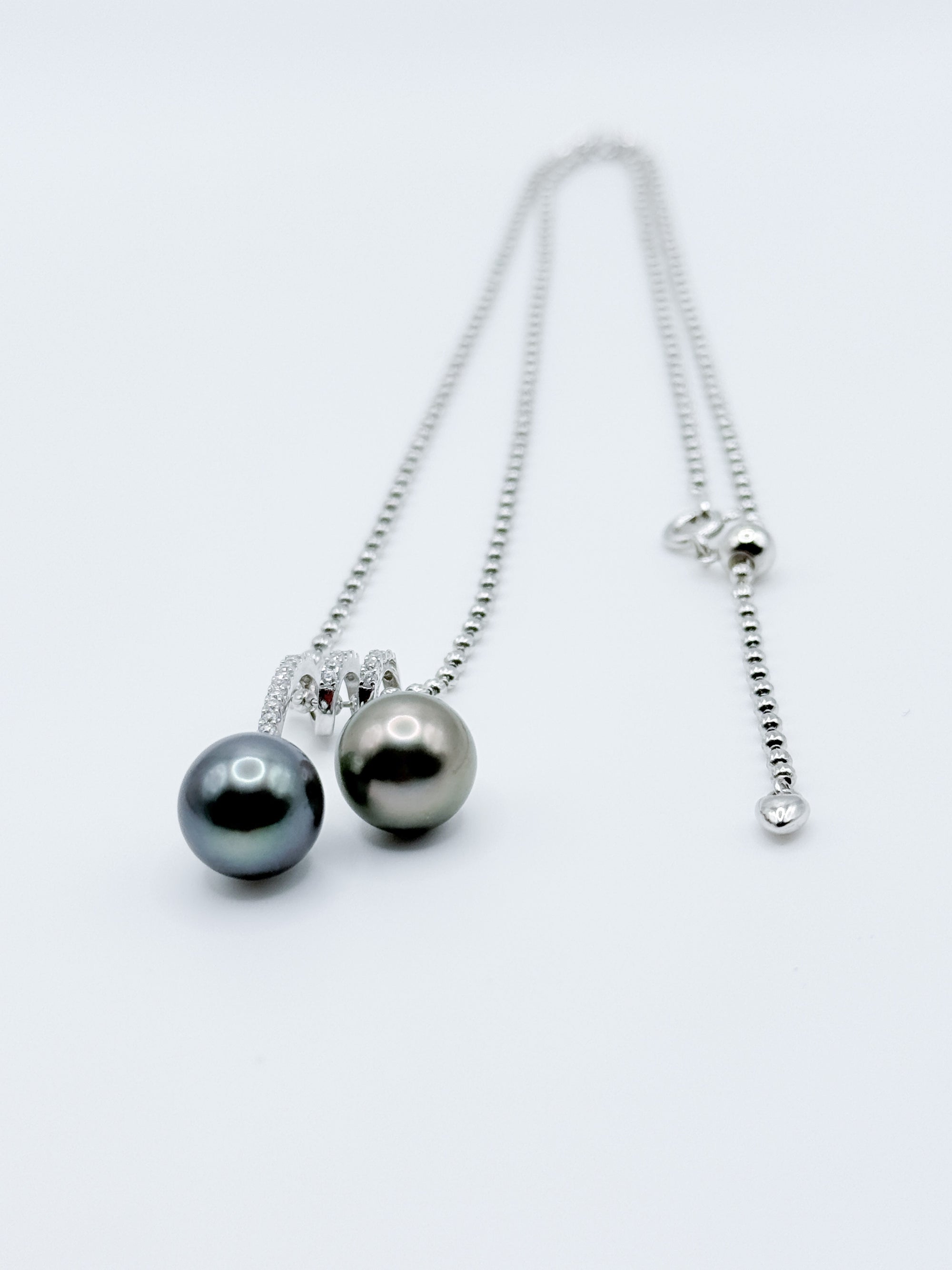 Double Tahitian pearl pendant necklace laid flat, showing sparkling CZ bail and adjustable silver ball chain.