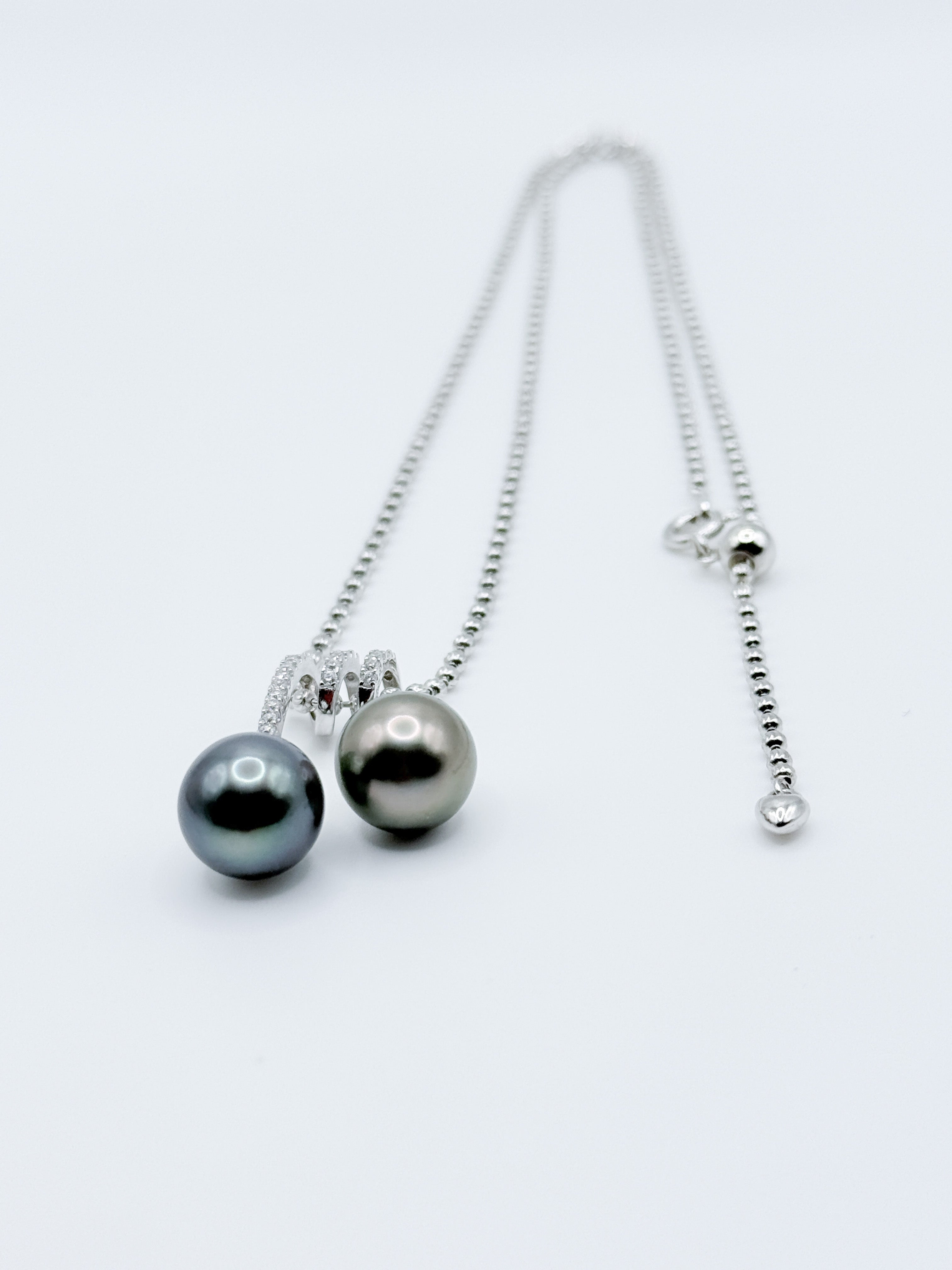 Double Tahitian pearl pendant necklace laid flat, showing sparkling CZ bail and adjustable silver ball chain.