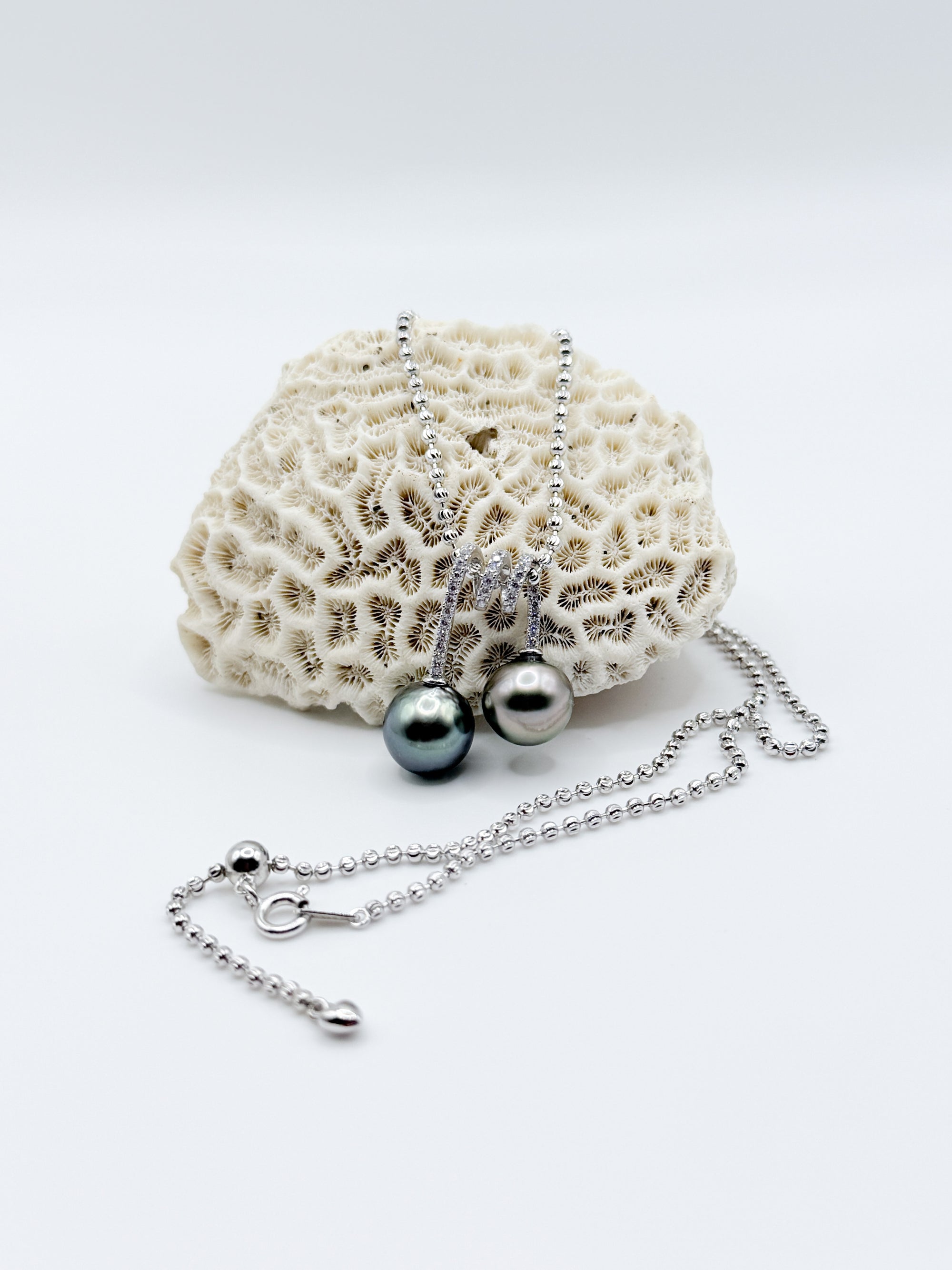 Two Tahitian pearls with CZ loops draped over coral, displayed with full view of silver chain.