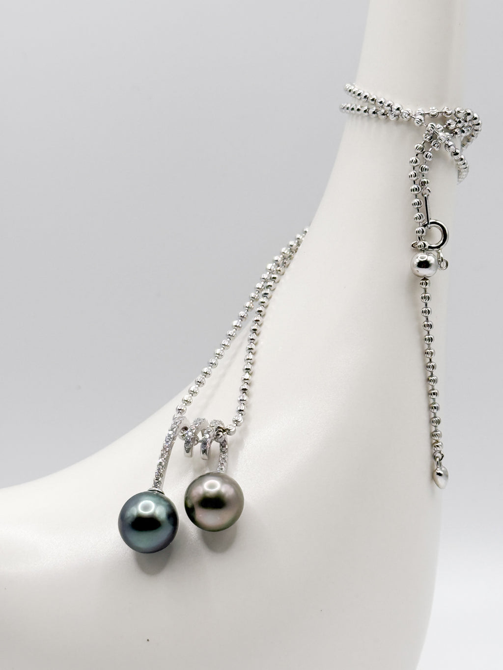 CZ-set double pearl pendant wrapped over ceramic bird neck, showing chain and clasp detail.