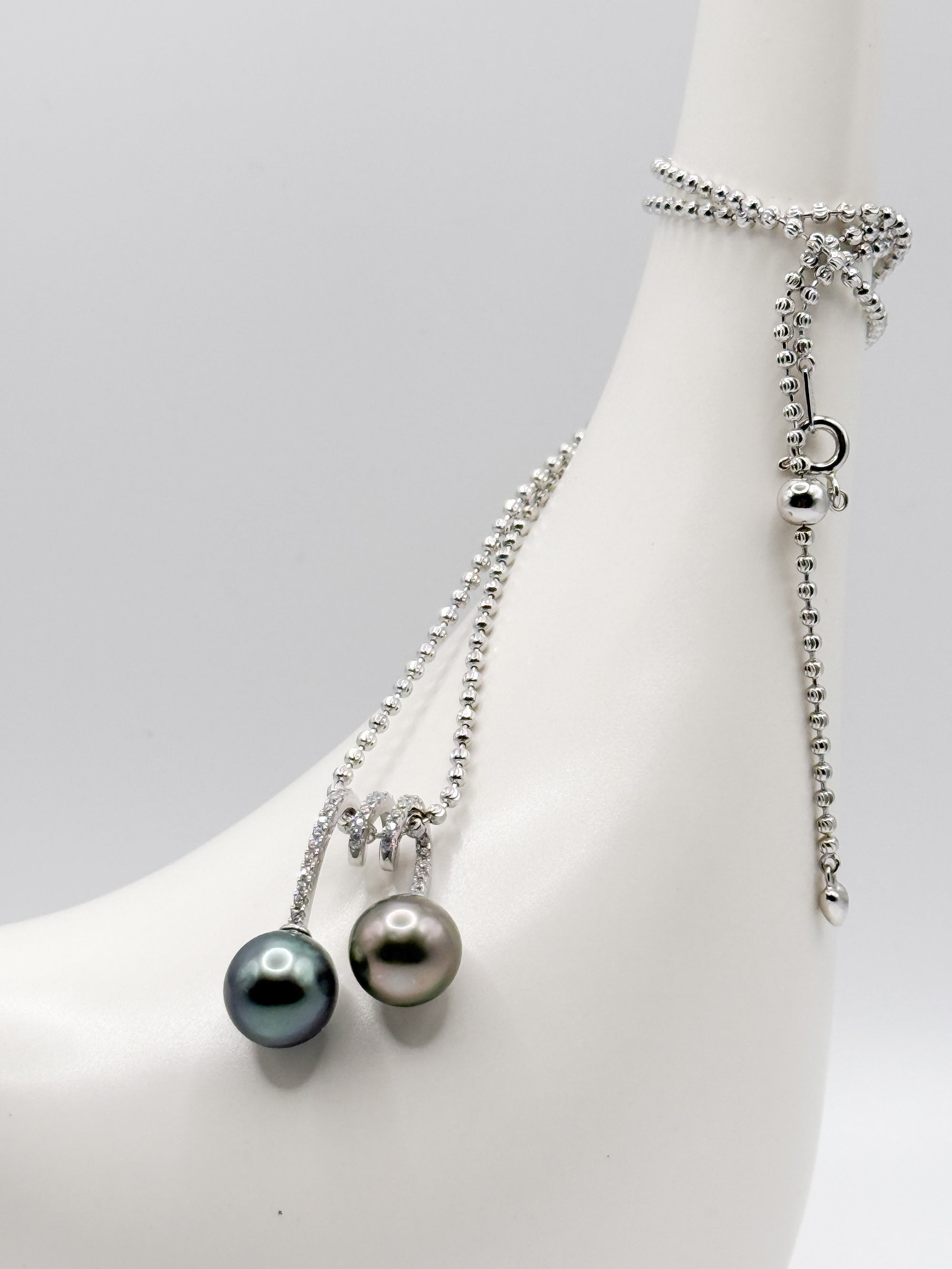 CZ-set double pearl pendant wrapped over ceramic bird neck, showing chain and clasp detail.