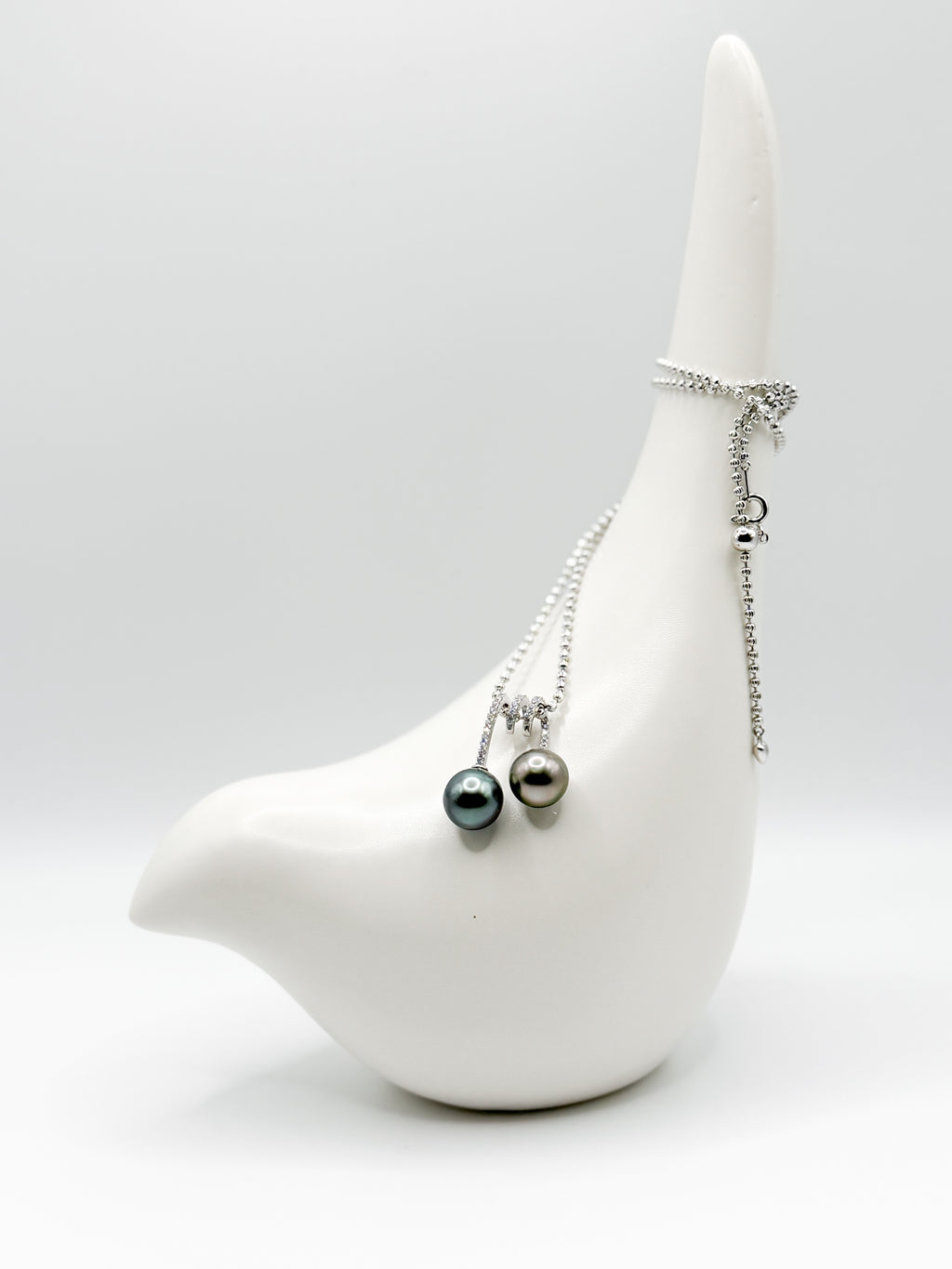 Long shot of necklace draped over ceramic bird with both pearls facing front in balanced composition.