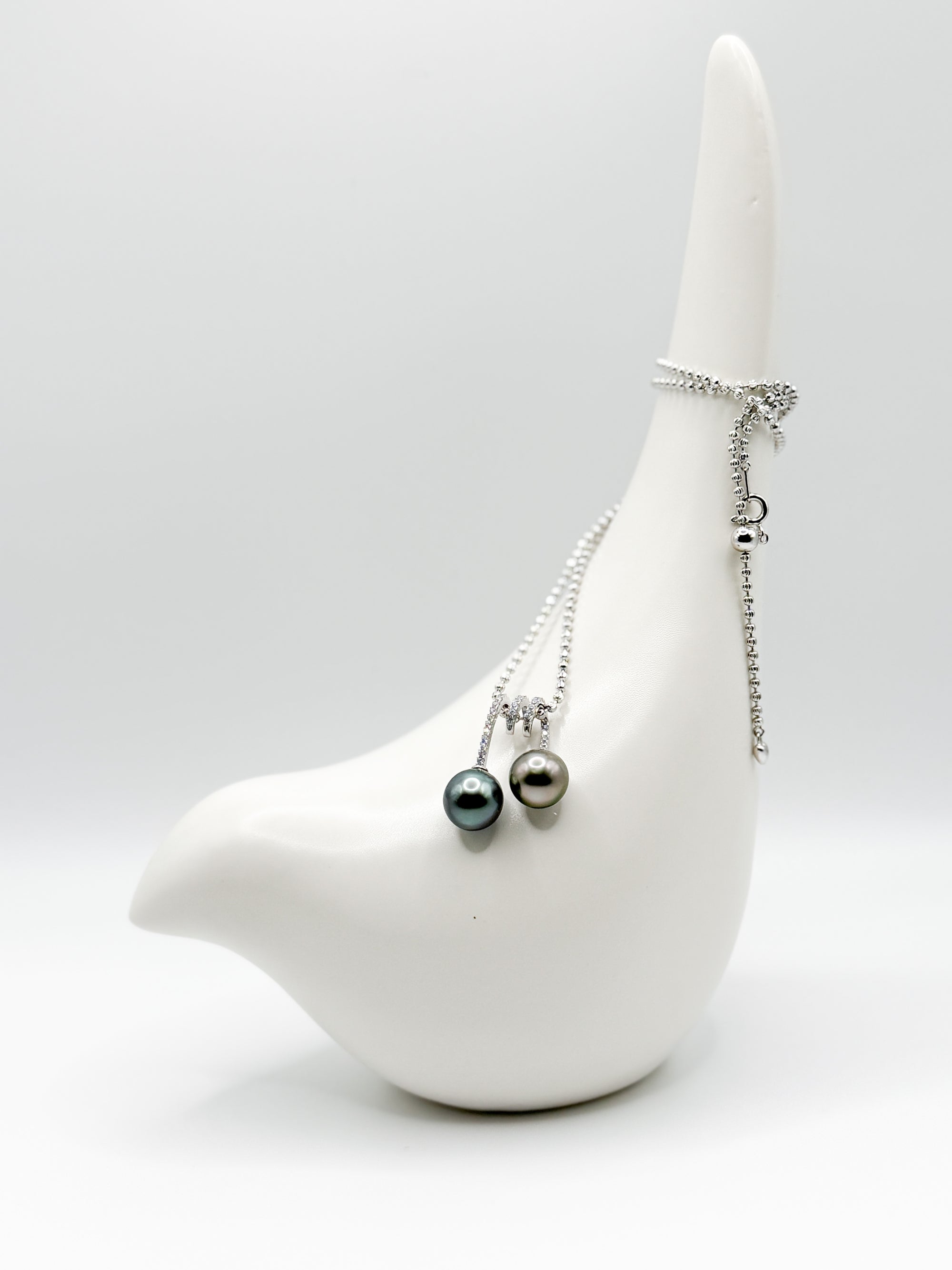 Long shot of necklace draped over ceramic bird with both pearls facing front in balanced composition.