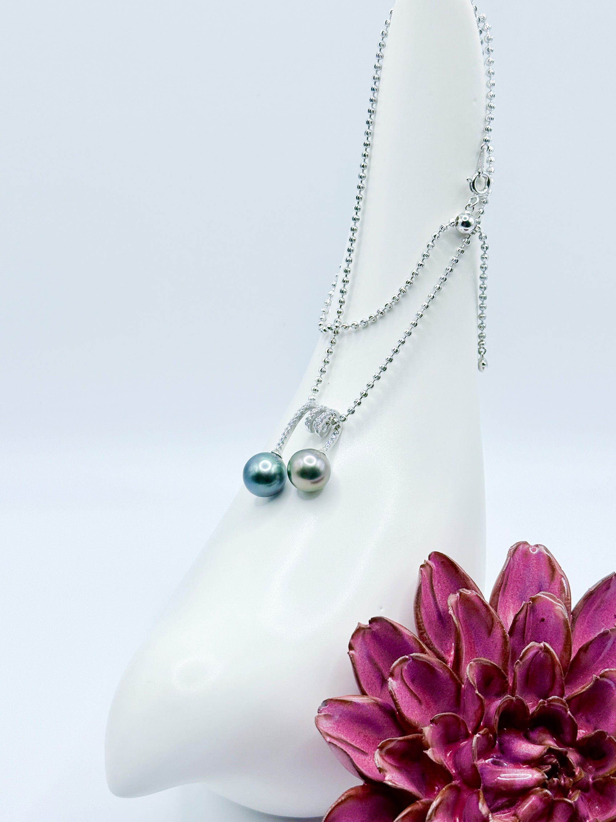 Double Tahitian pearl pendant styled on ceramic bird and red flower, with chain draped elegantly.