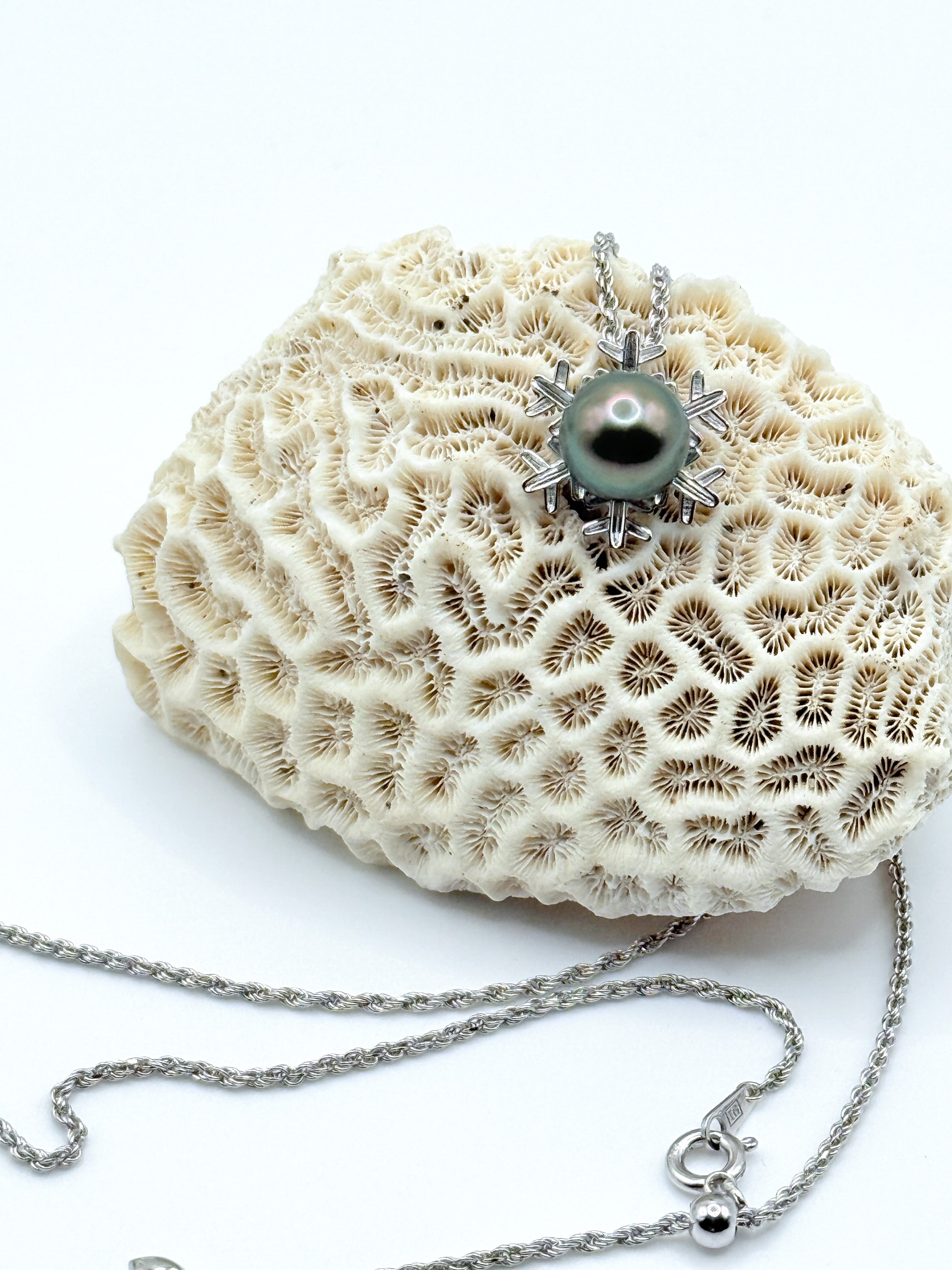 Close-up of a platinum-toned Tahitian pearl set in a sterling silver snowflake pendant, shown against a neutral background.