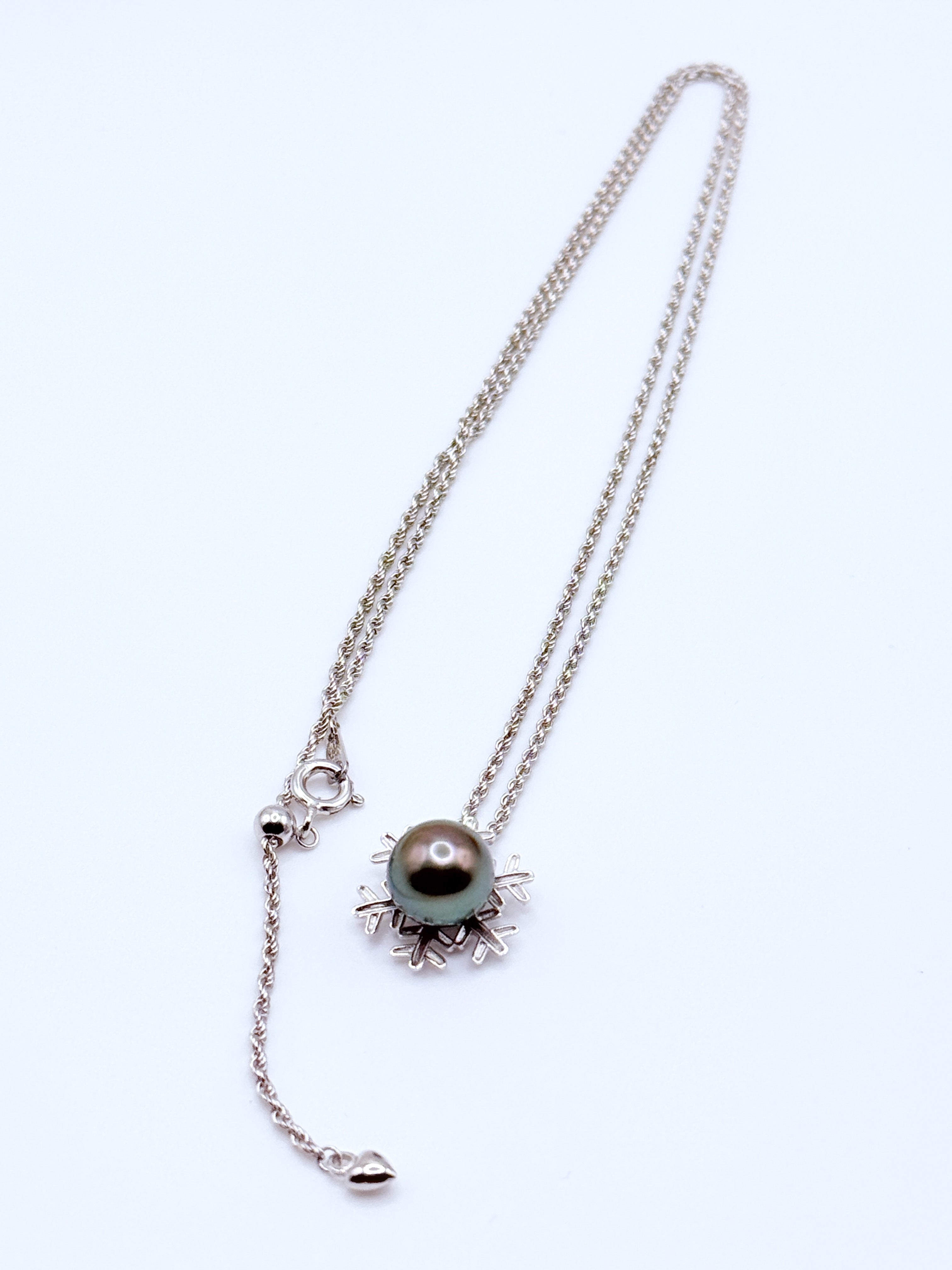 Angled view highlighting the iridescent green overtone and orient of the Tahitian pearl within the intricate snowflake setting.