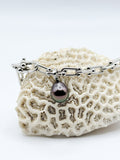 Sterling silver chain bracelet with Tahitian pearl charm draped over white coral specimen, highlighting the contrast between the dark pearl and textured coral surface