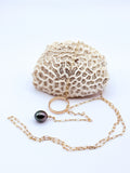 Gold chain lariat necklace with dark Tahitian baroque pearl charm displayed with white coral specimen on light background