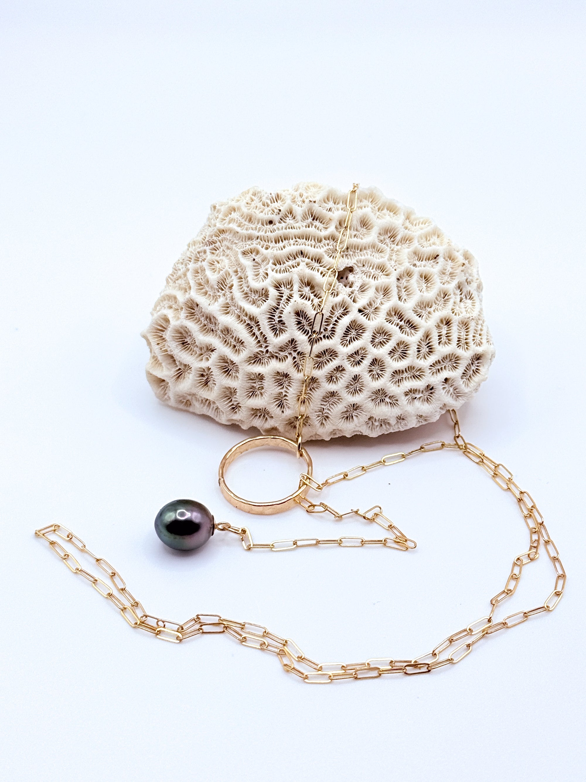 Gold chain lariat necklace with dark Tahitian baroque pearl charm displayed with white coral specimen on light background
